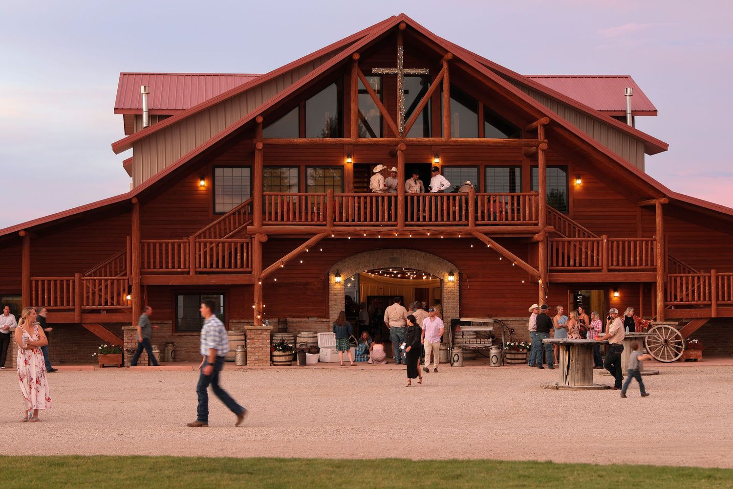The Barnsion in Harlowton, MT. A Rustic wooden lodge with red roof and wrap-around deck where guests gather and mingle at a wedding.