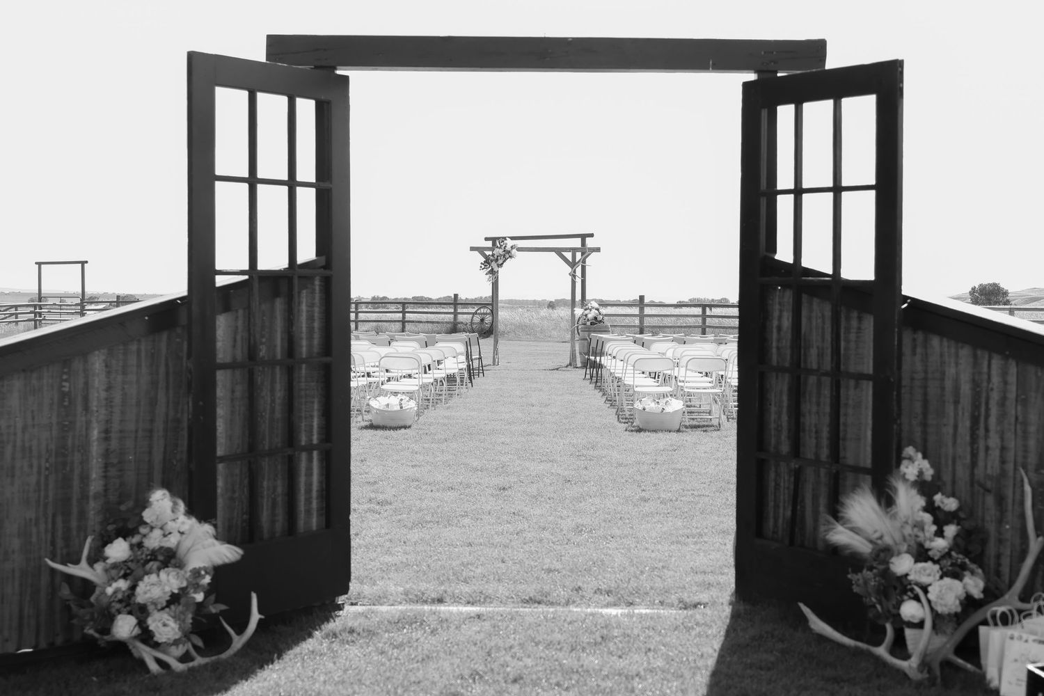 A black and white wedding venue entrance shows open doors leading to an outdoor ceremony setup with meadow and mountain views.