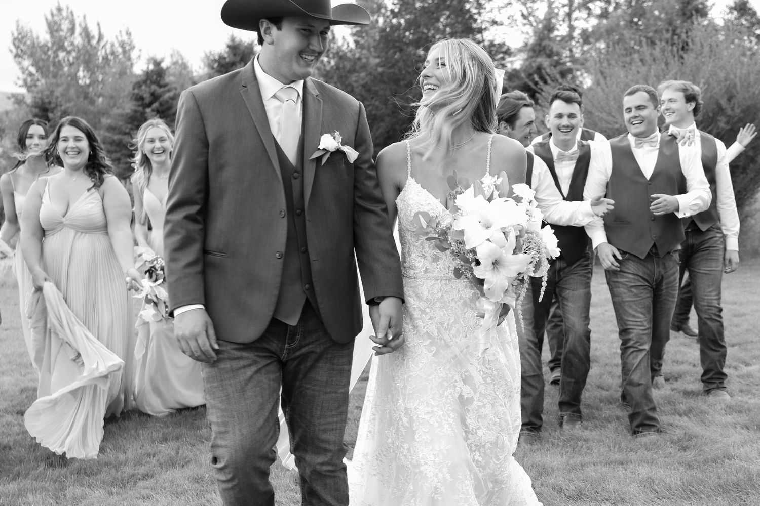 A Montana Western style wedding couple walking outdoors with bridal party in black and white photography.