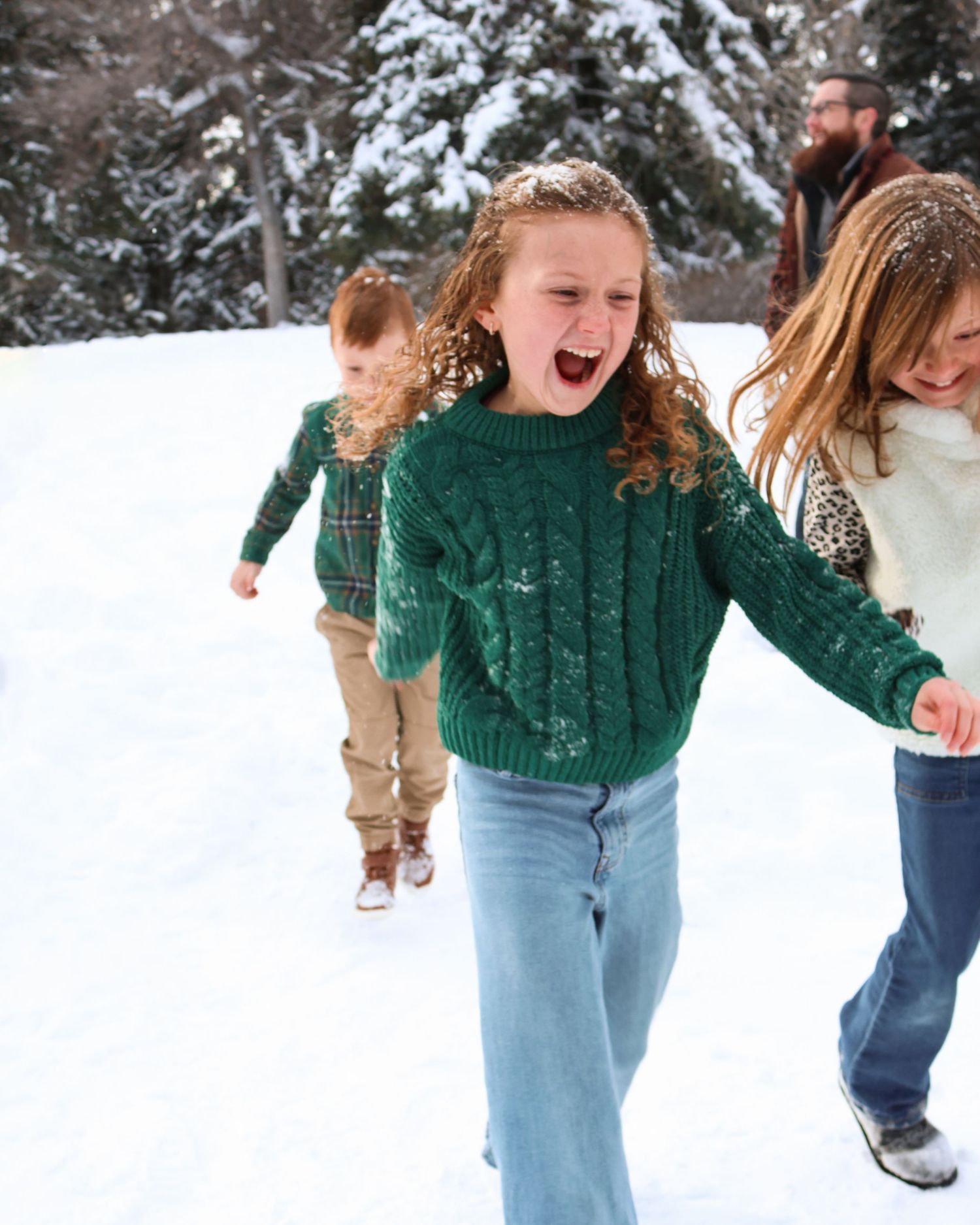 People in cozy winter sweaters enjoy playing together in a snowy landscape with snow-covered trees in the background.
