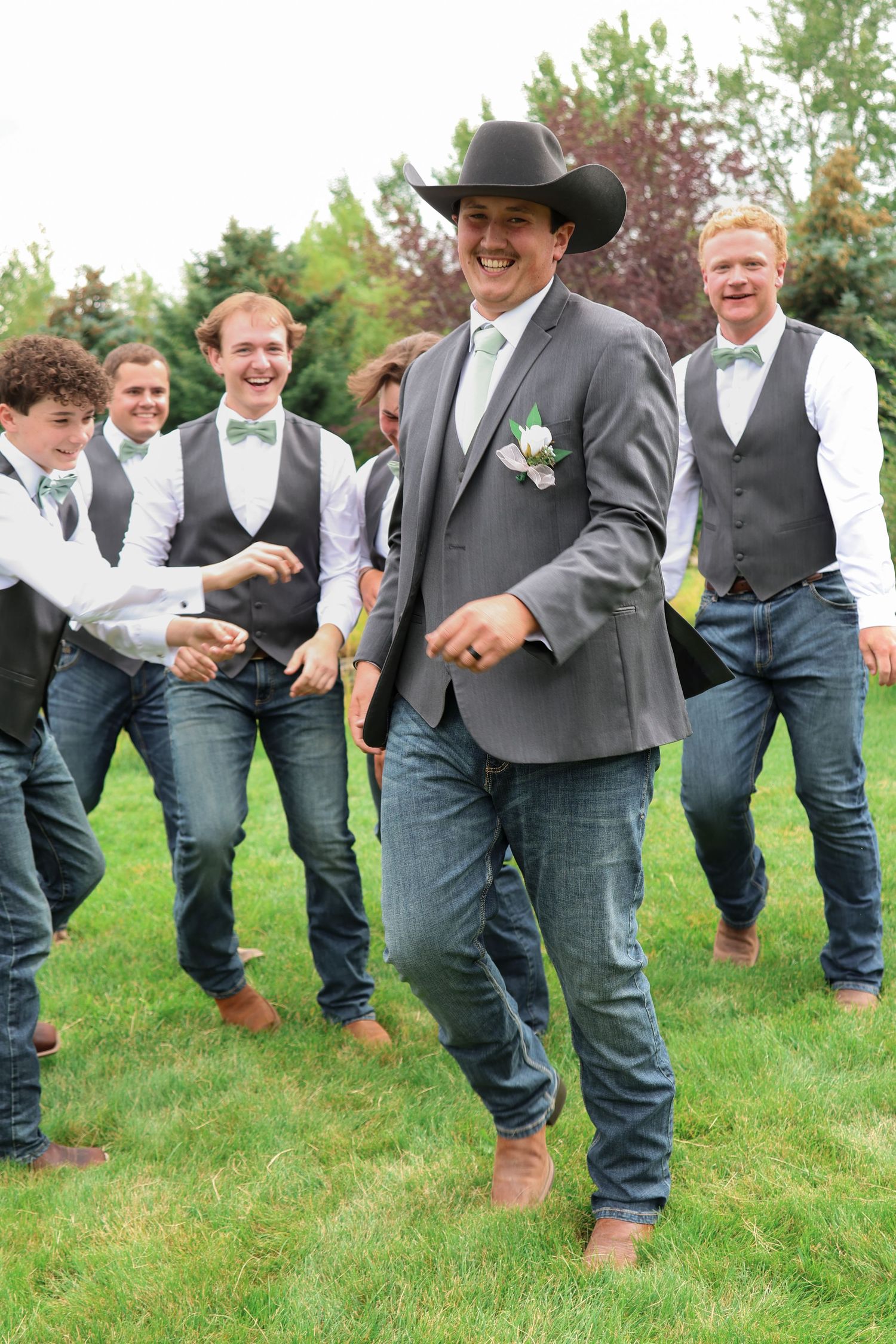 A Montana western-style wedding party with groomsmen wearing jeans and cowboy hats celebrating outdoors.