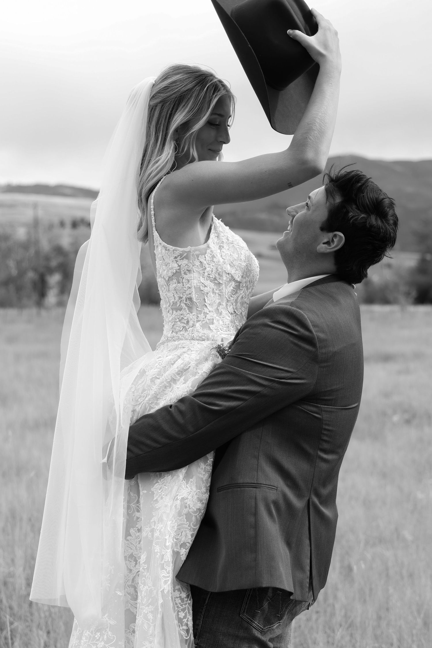 A romantic black and white wedding photo of newlyweds dancing together in a field with Montana's mountains in the background.