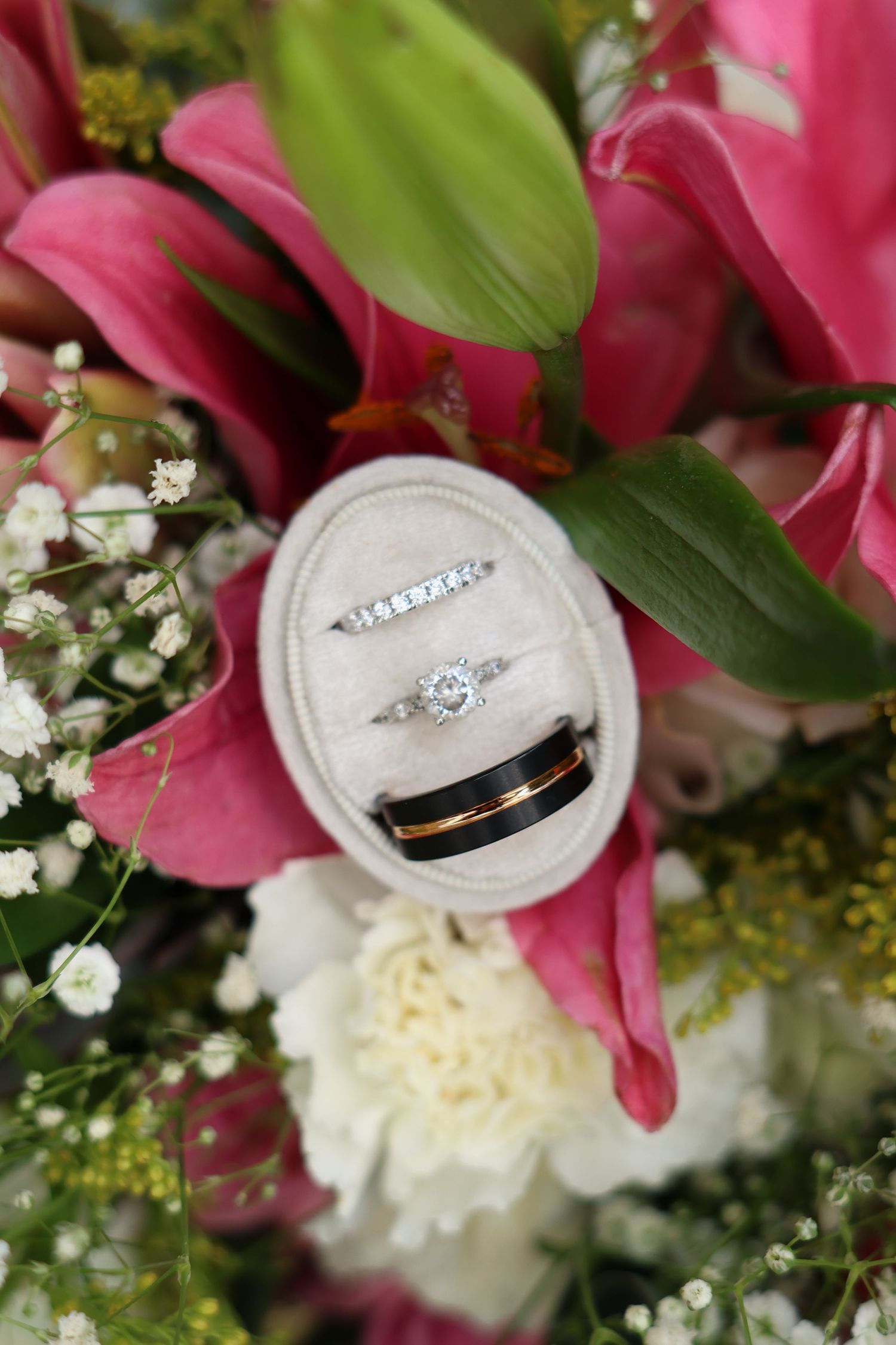 Wedding rings nestled among pink lilies and white flowers in a romantic floral arrangement.