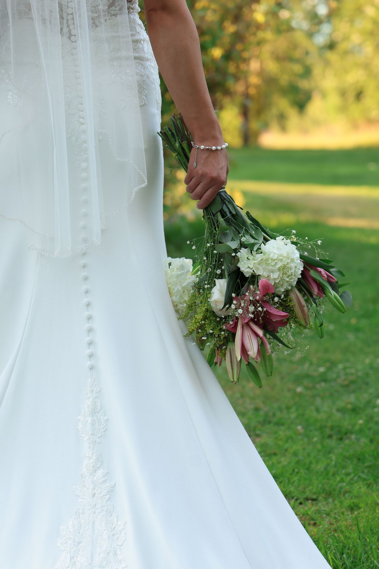 Wedding photography detail showing bridal bouquets with white and pink flowers against lush green grass.