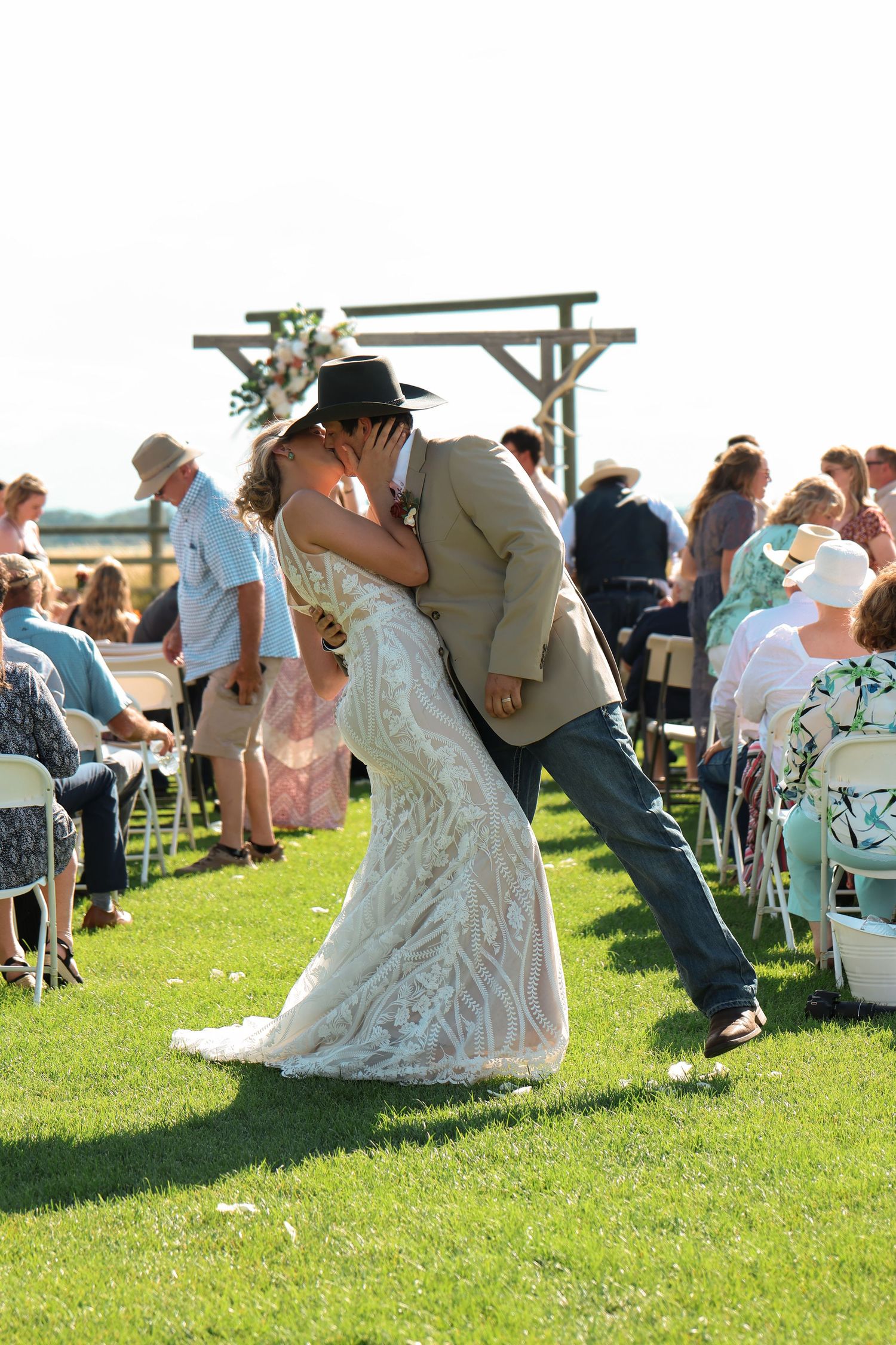 A couple performs an elaborate dipping kiss move on a grassy lawn during an outdoor wedding ceremony.