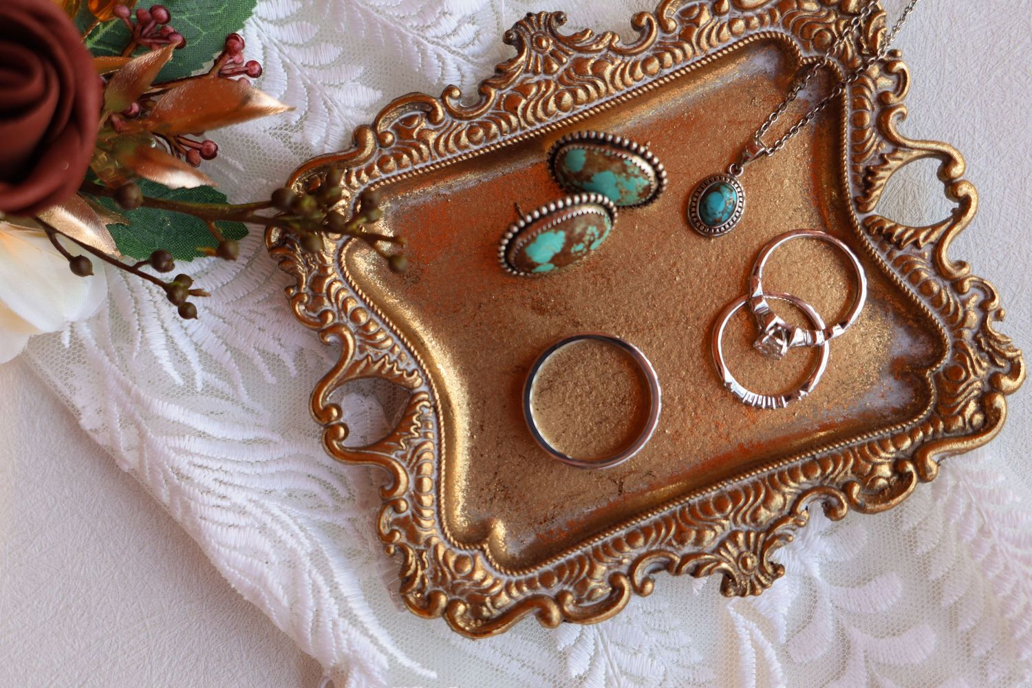 Wedding rings and turquoise jewelry displayed on an ornate vintage gold tray with decorative edges.