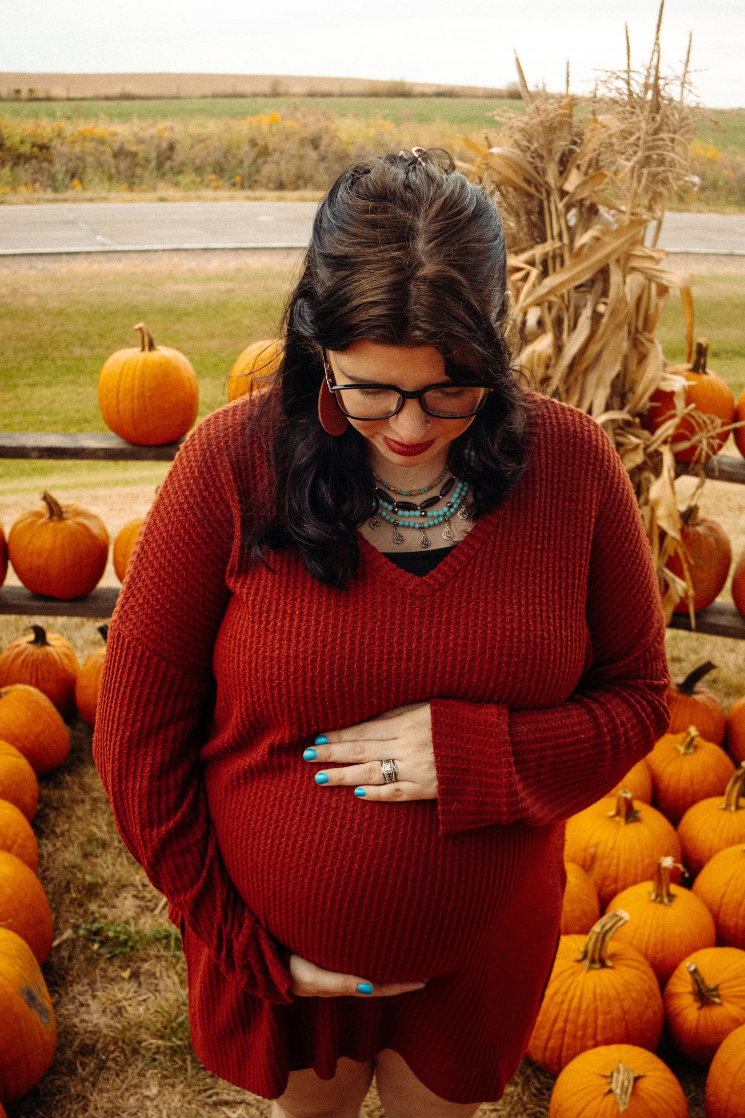 Person in red sweater sitting among pumpkins at an autumn harvest display.
