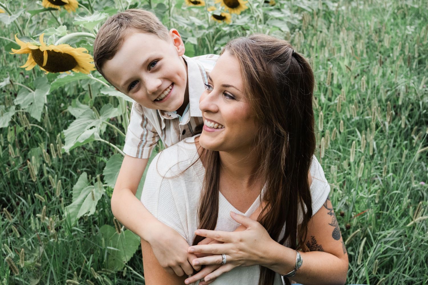 A mother and son embraces and laughs together in a sunflower field during a summer photoshoot.