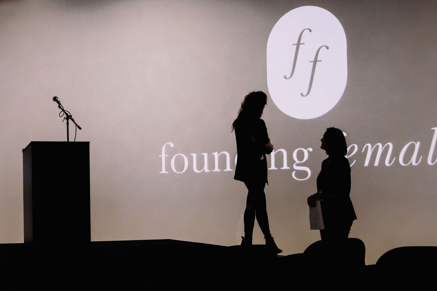 Silhouettes of people against a light projection screen in a dark room during a presentation.