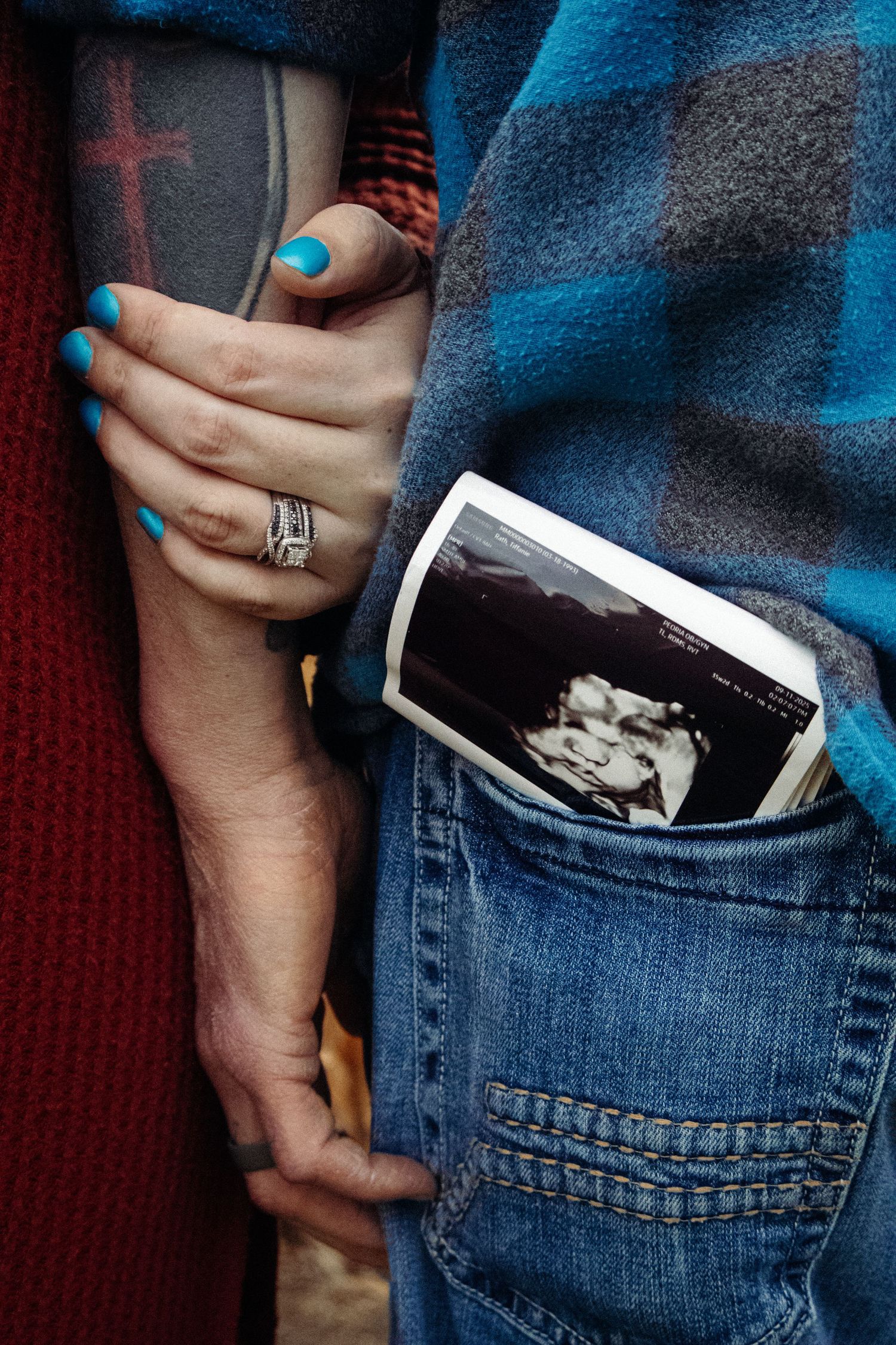 Close-up of hands holding an ultrasound photo tucked into a denim pocket.