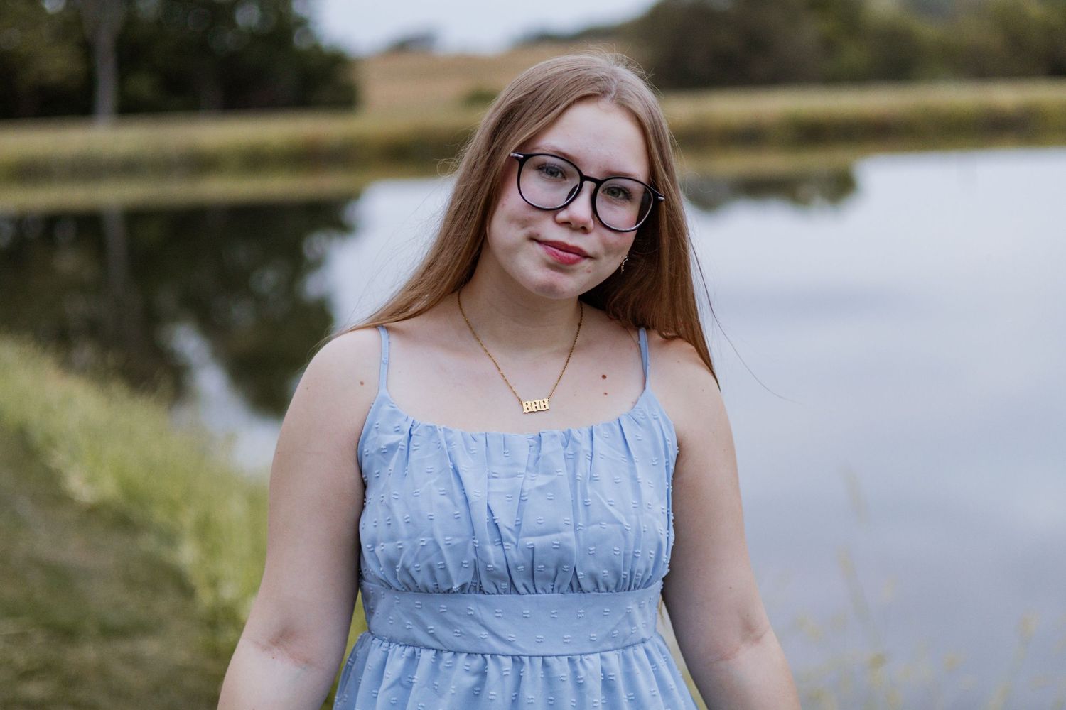 Person in light blue dress sitting by waterfront on sunny day.