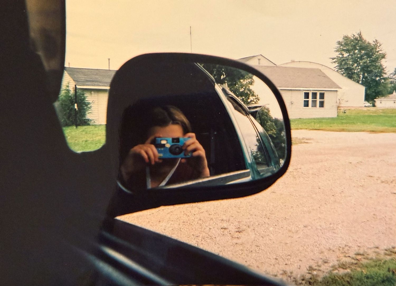 View through car side mirror showing reflection of rural landscape.