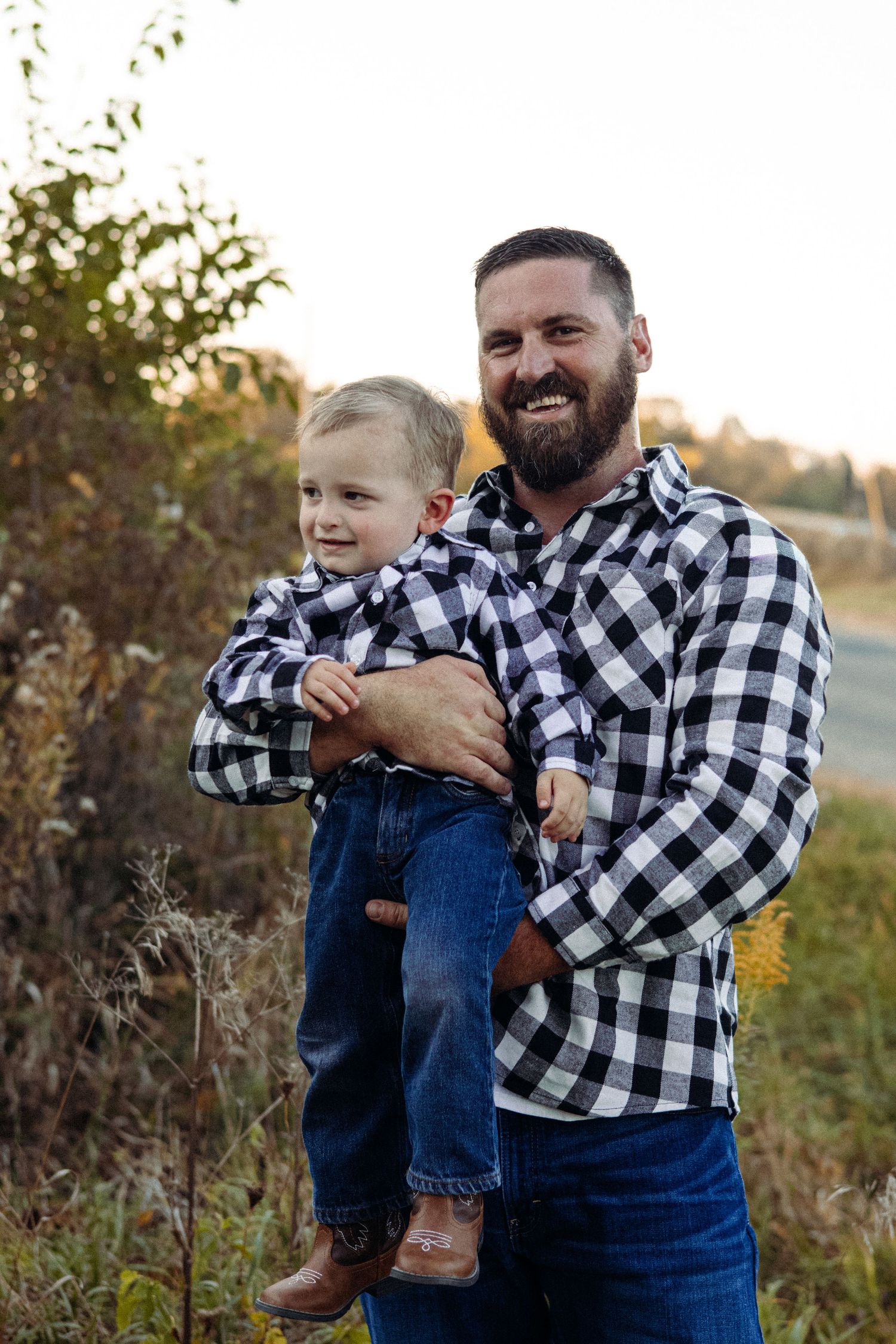 Parent and child in matching buffalo plaid shirts and overalls laughing together outdoors.