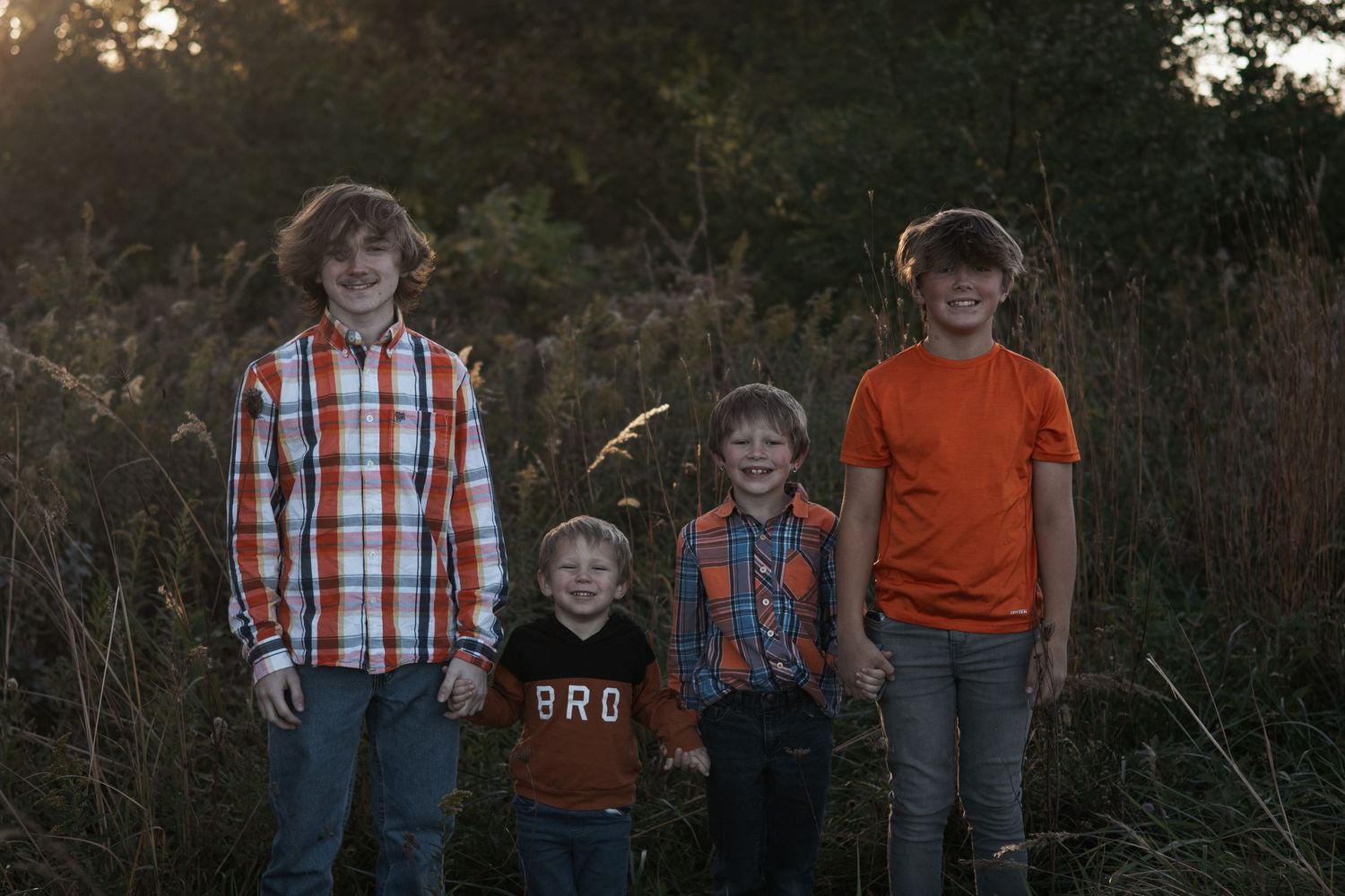 Four siblings stand together at sunset wearing coordinated orange and plaid outfits.