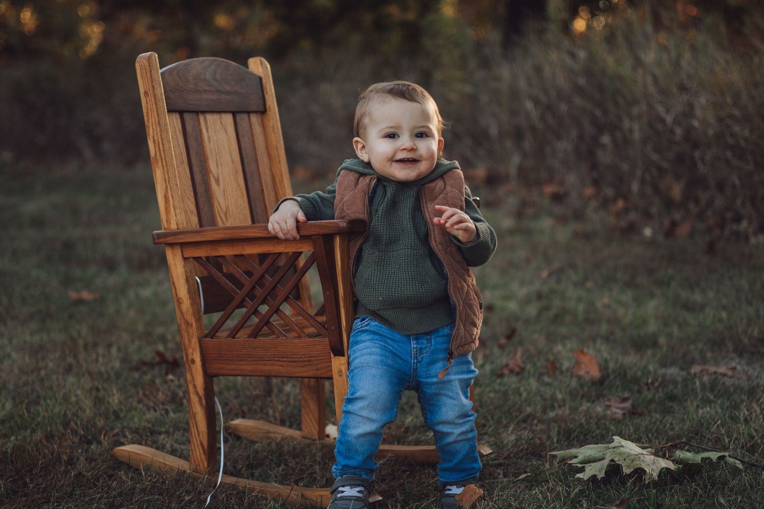 Wooden rocking chair placed in outdoor setting with fall foliage in background.