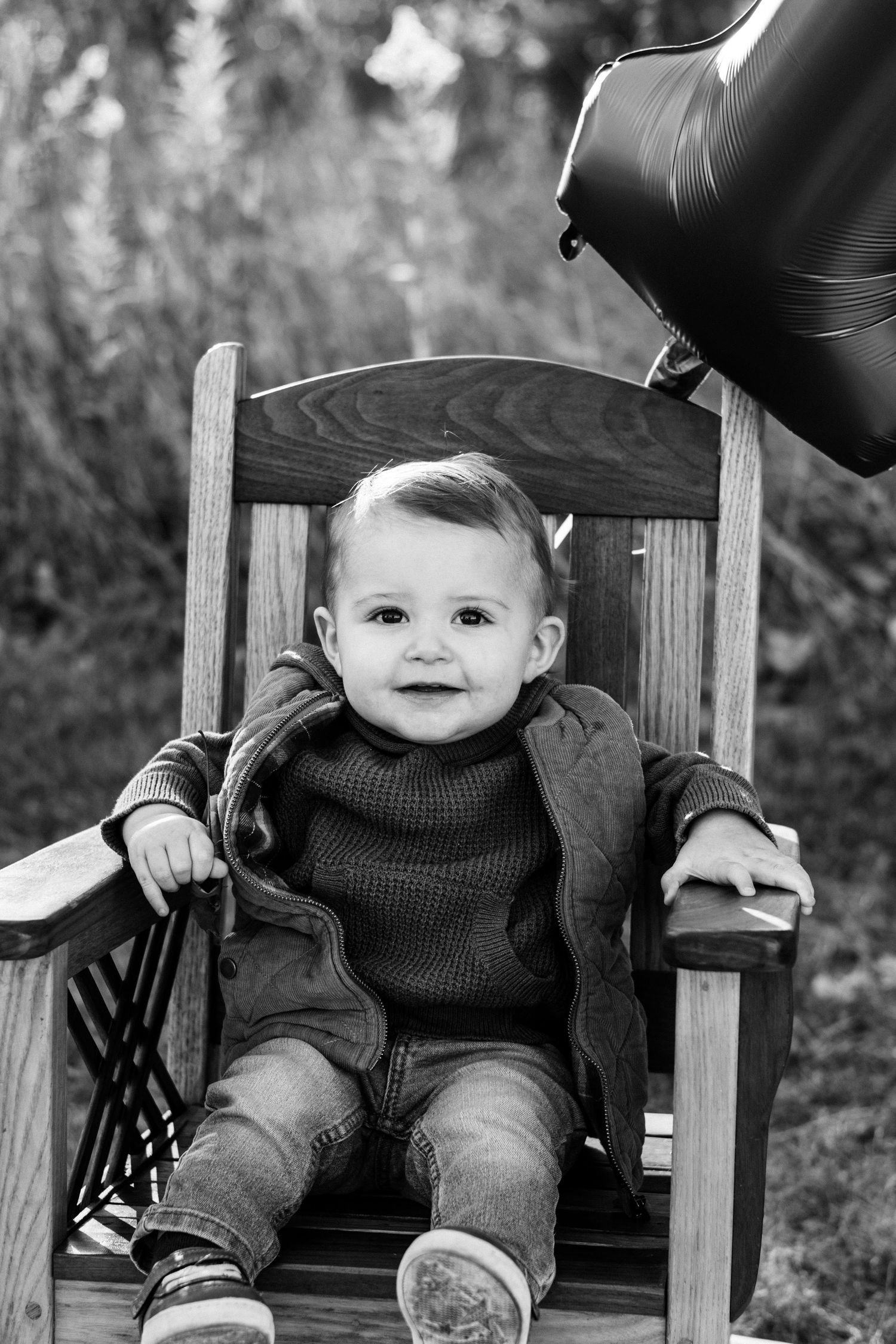 Black and white photo of a baby sitting in a wooden chair.