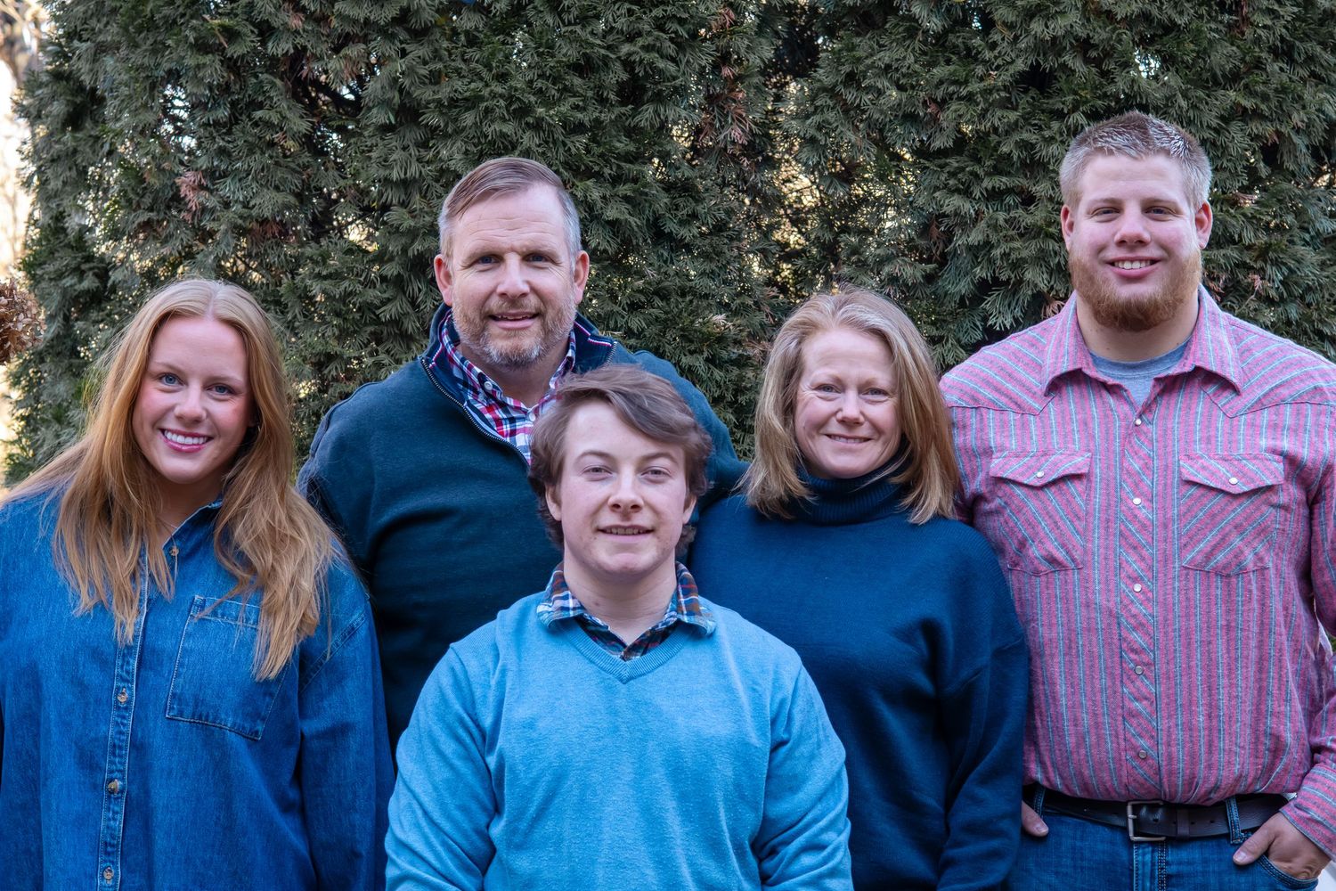 A family of five poses together for a portrait against a green hedge background.