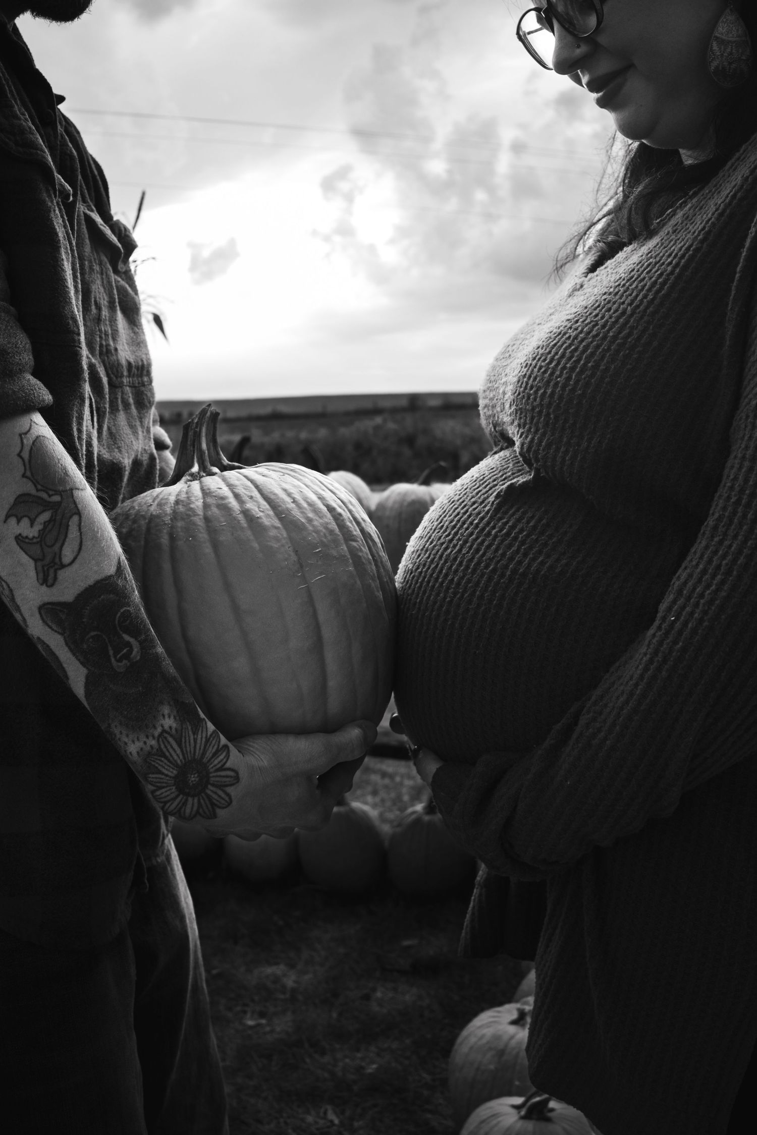 Black and white photo of someone in a knit sweater sitting near pumpkins.