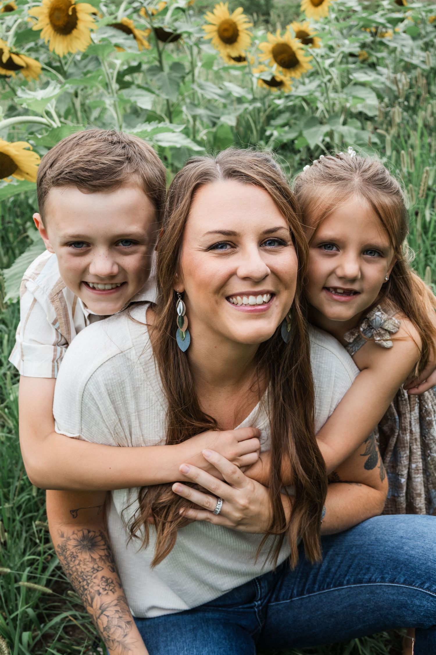 Family embracing and laughing together in sunflower field on sunny day.