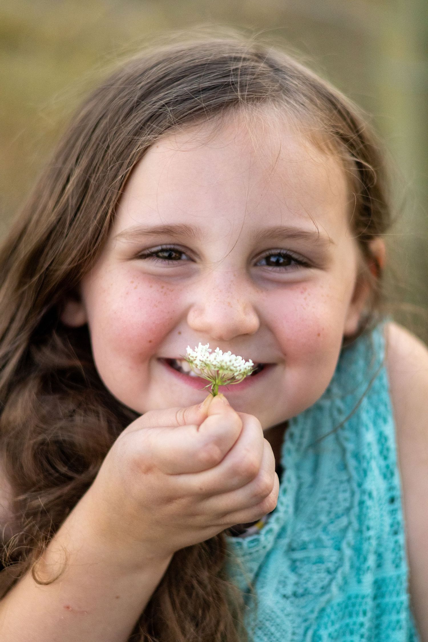 A playful photo shows a child with a flower on their nose in a whimsical outdoor portrait series.