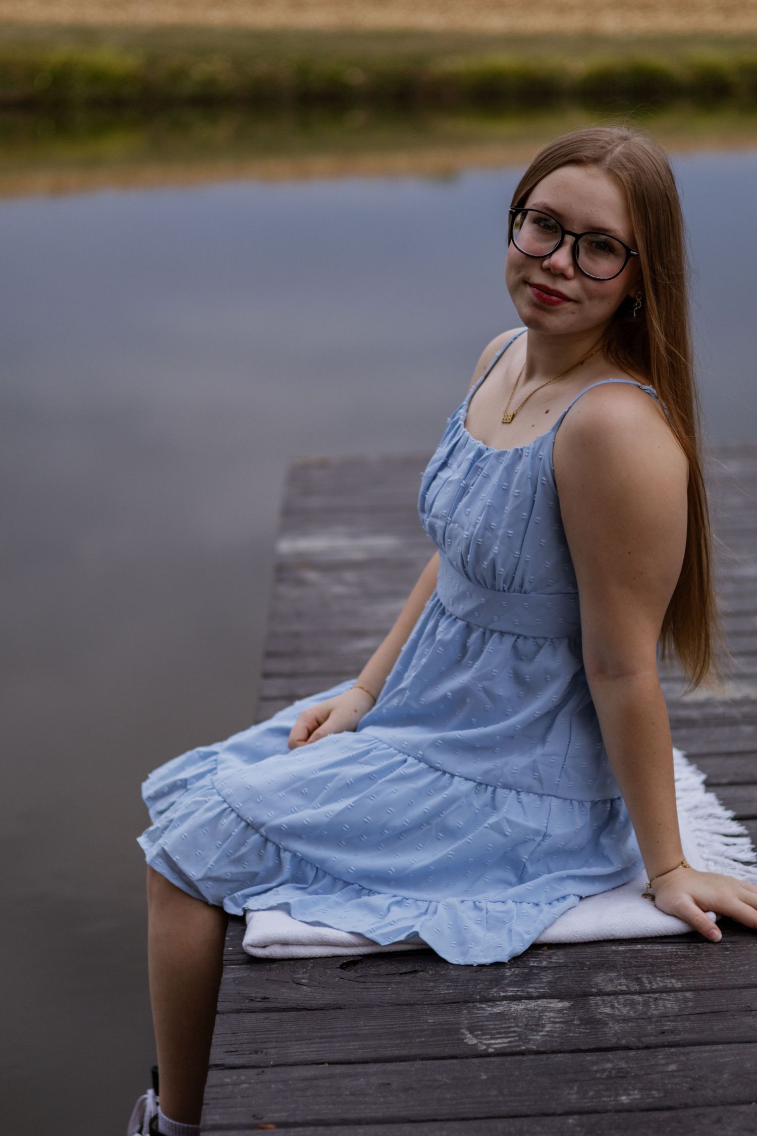 Person in light blue dress sitting on wooden dock by calm water in multiple poses.