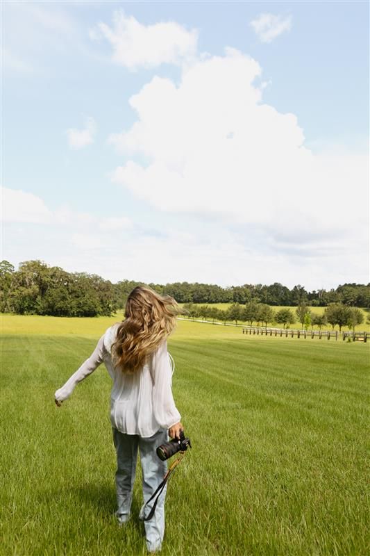 Person twirling in white dress and jeans through a vast green meadow.