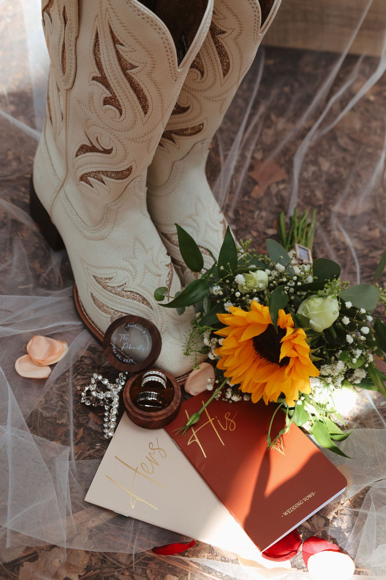 Wedding details featuring white cowboy boots, sunflowers, and delicate floral arrangements on a marble surface.