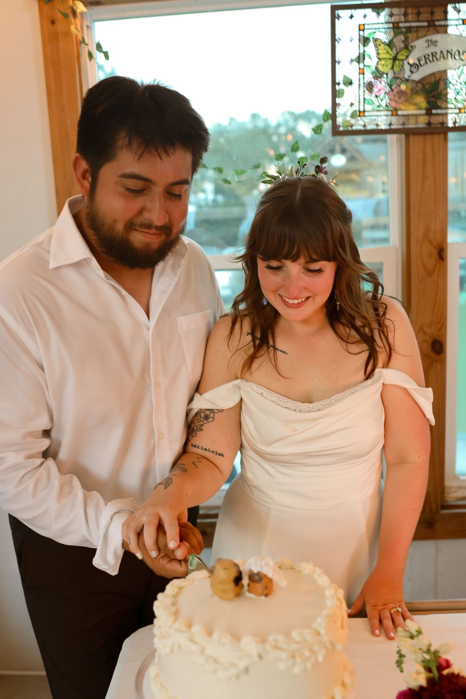 Bride and groom cutting their white wedding cake together, smiling joyfully at their reception.