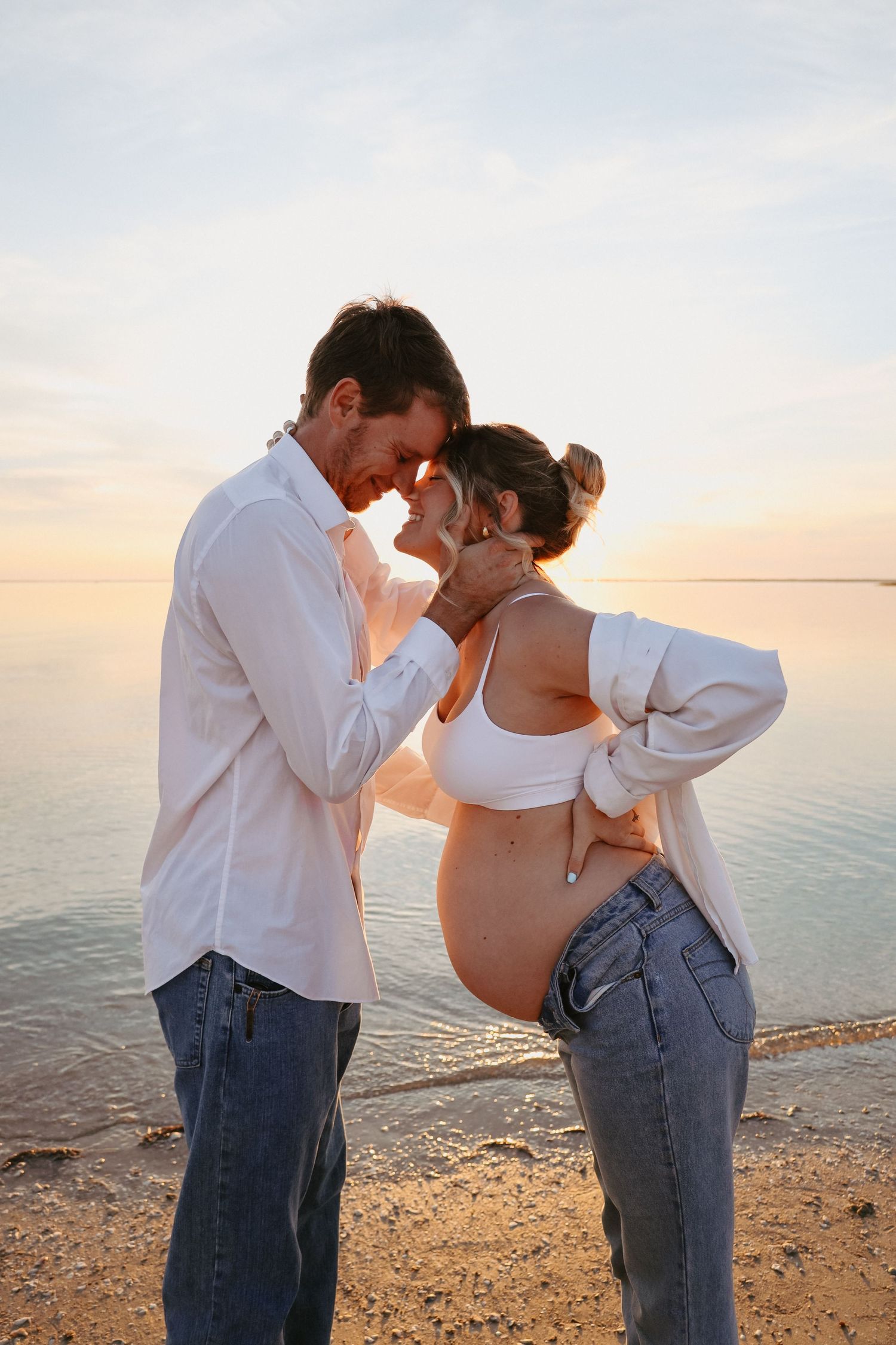 An expecting couple shares tender moments during a sunset beach photoshoot.