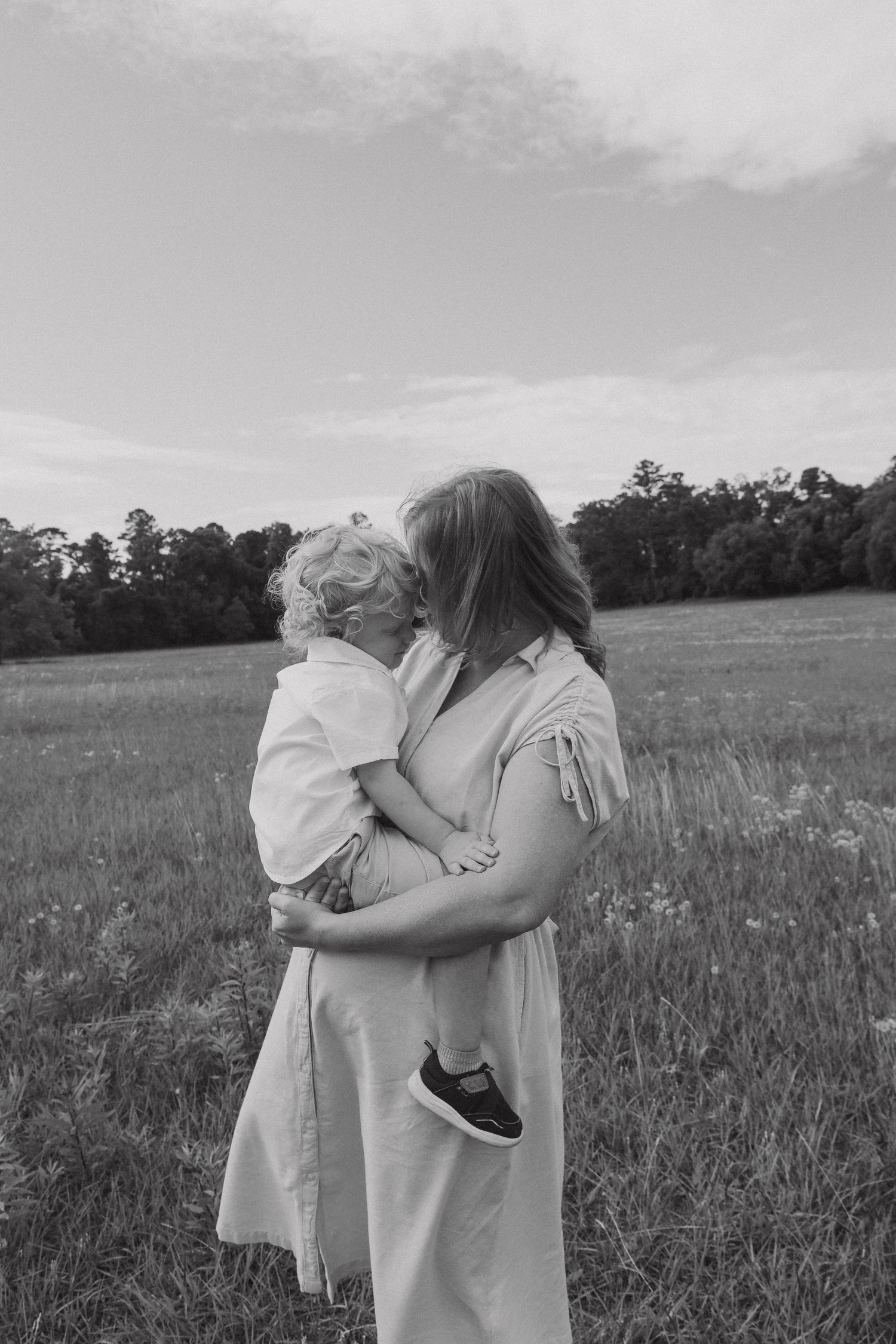 A tender embrace captured in black and white across a serene meadow landscape.