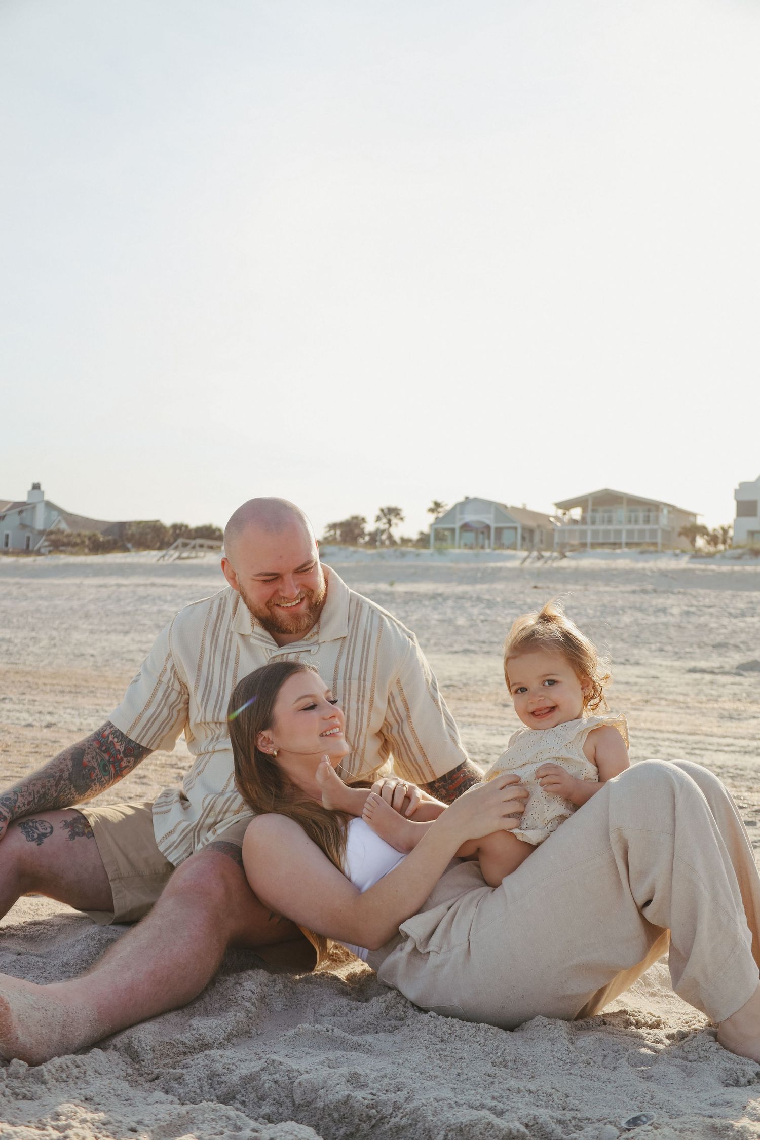 Family enjoys playful moments together while lying on beach sand at sunset.