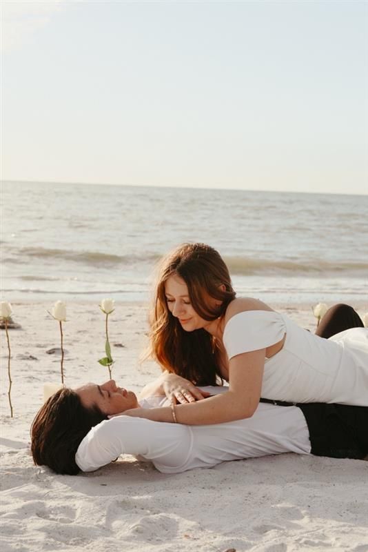 A couple lies together on white sand beach at sunset in romantic poses.