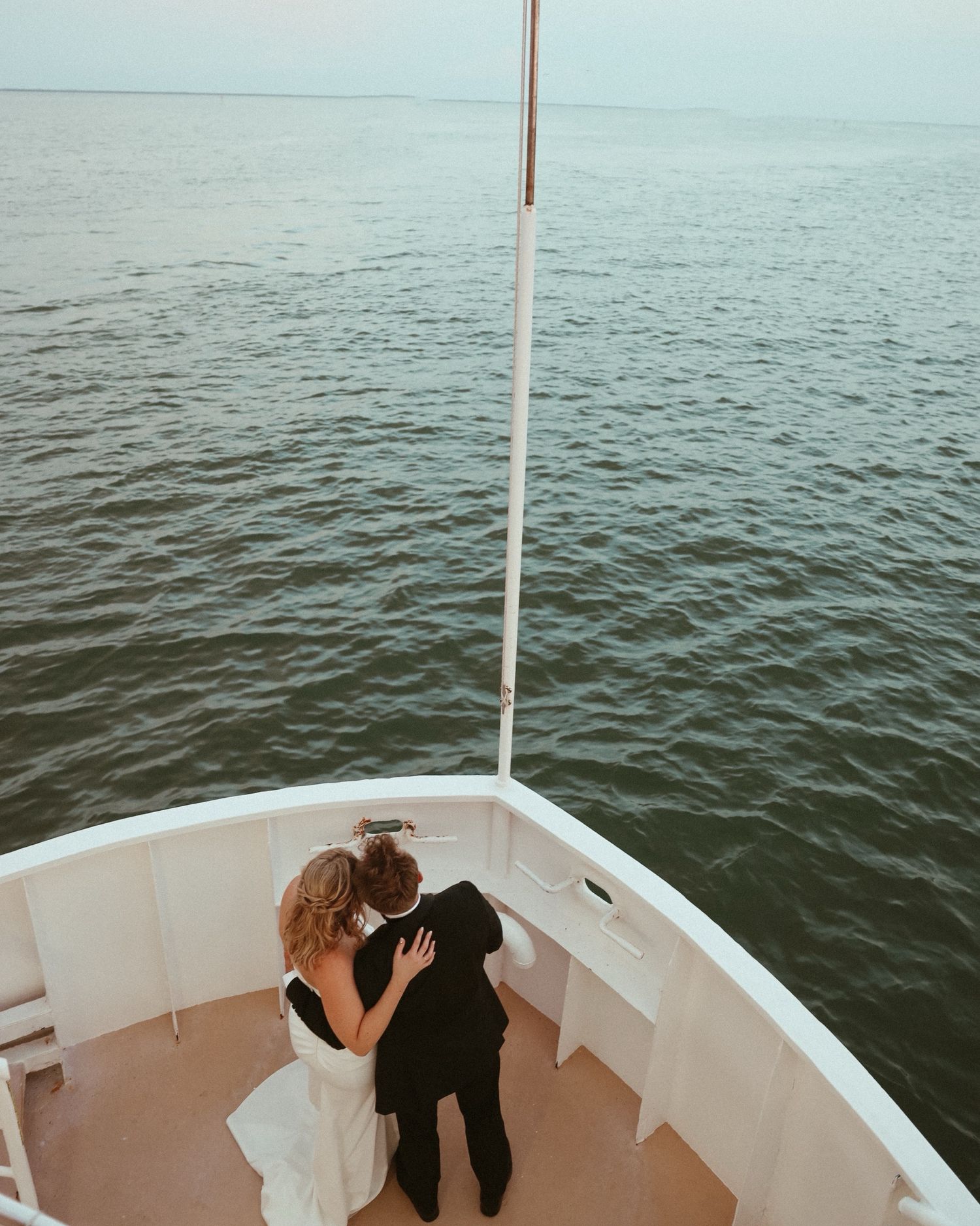 Couple embraces on white boat deck with serene ocean waters in background.