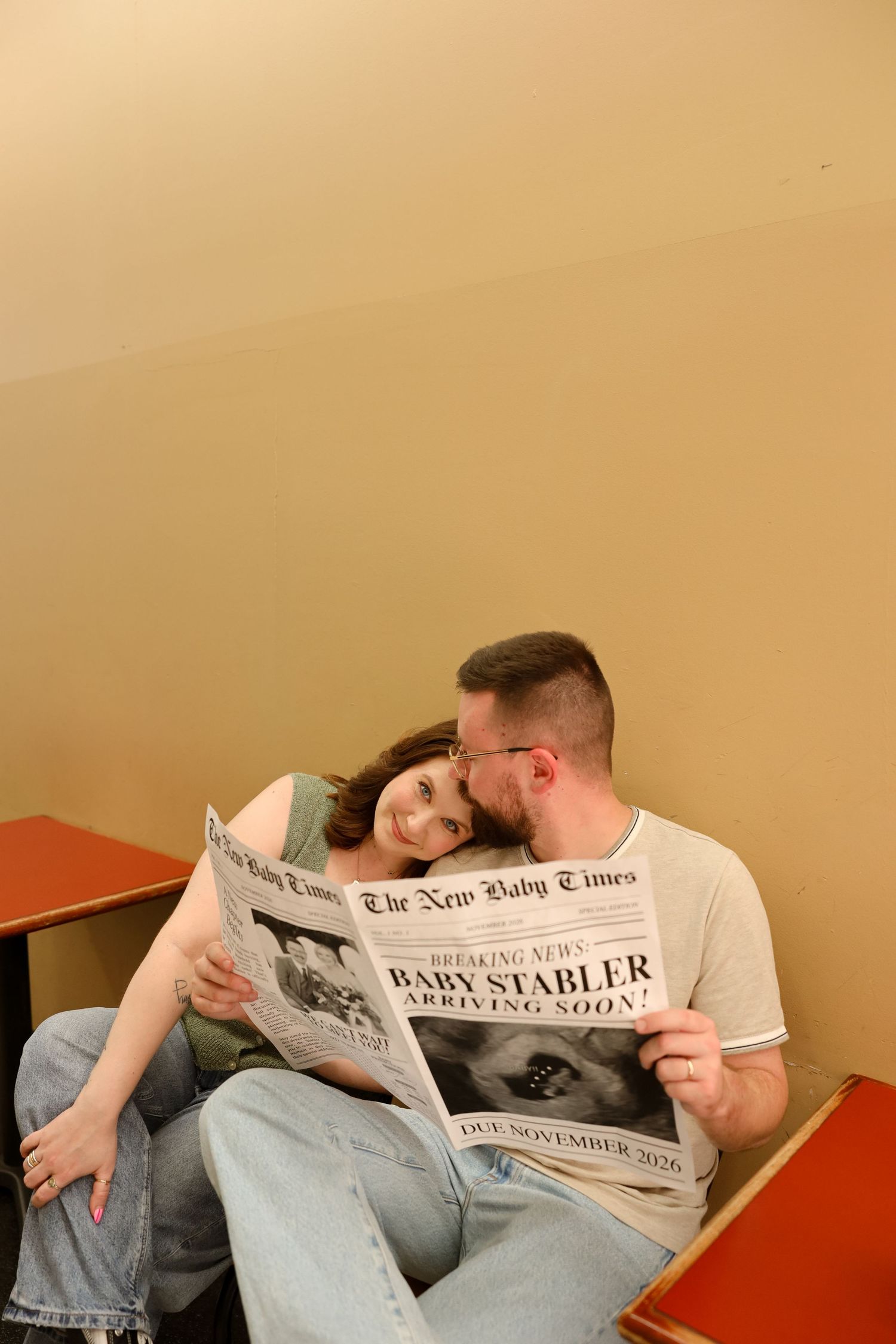 Couple sitting together reading a newspaper announcing Baby Stabler arriving soon, sharing a tender moment.