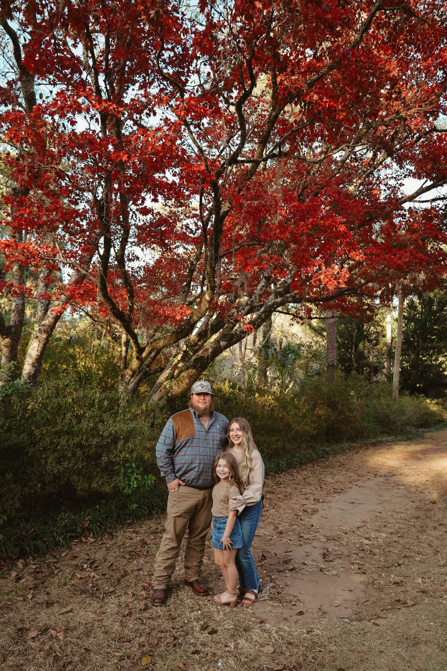 A dirt path winds through vibrant red autumn foliage with trees creating a natural tunnel effect.