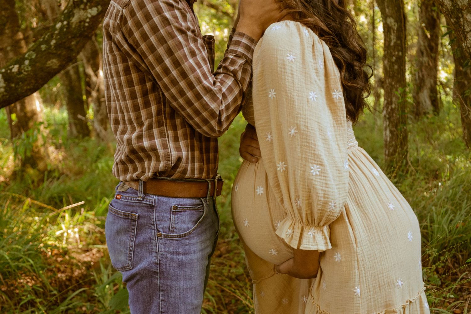 A romantic couple embracing in a sunlit forest wearing casual clothing.