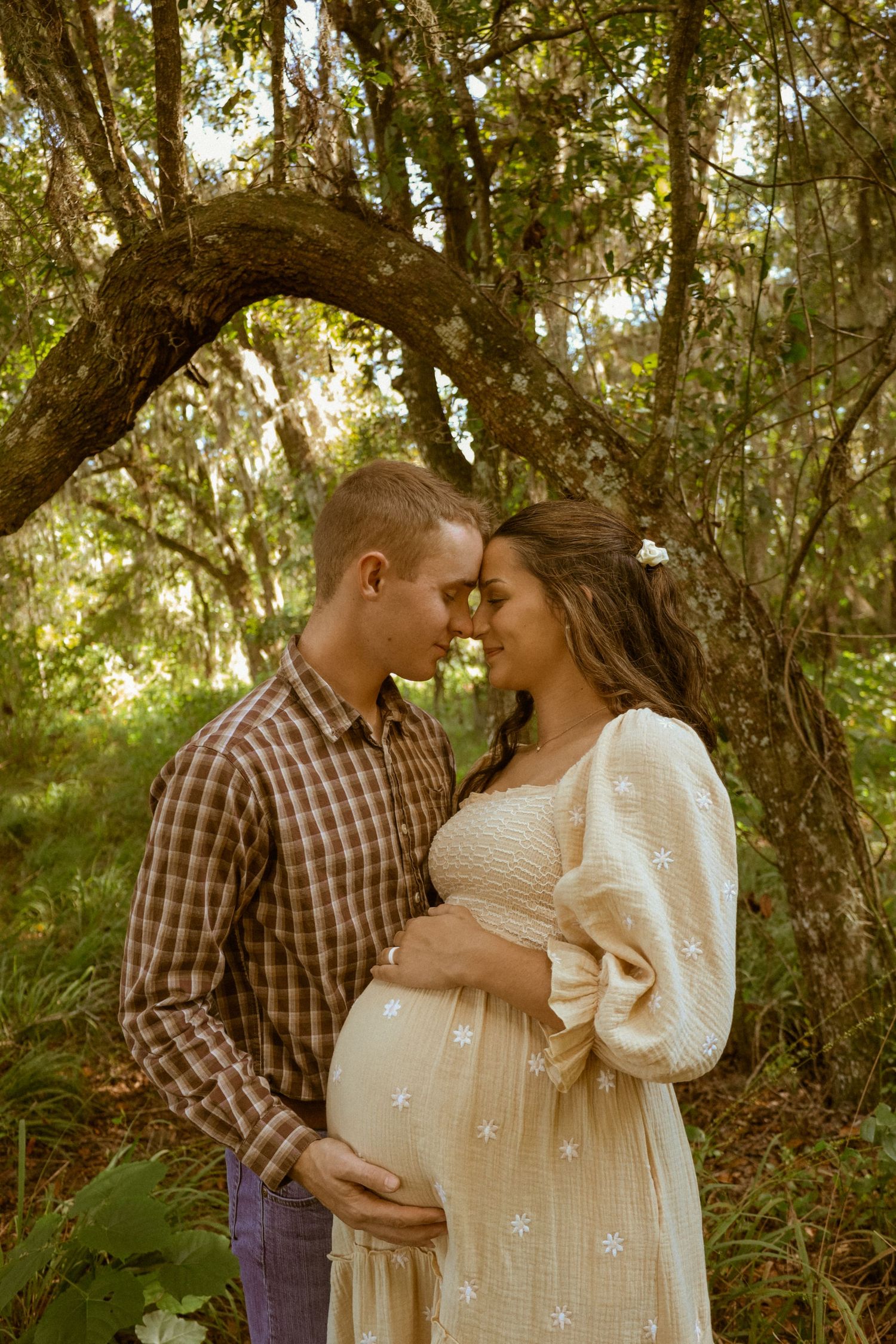 Couple shares intimate moments in sequence among sunlit trees and greenery.