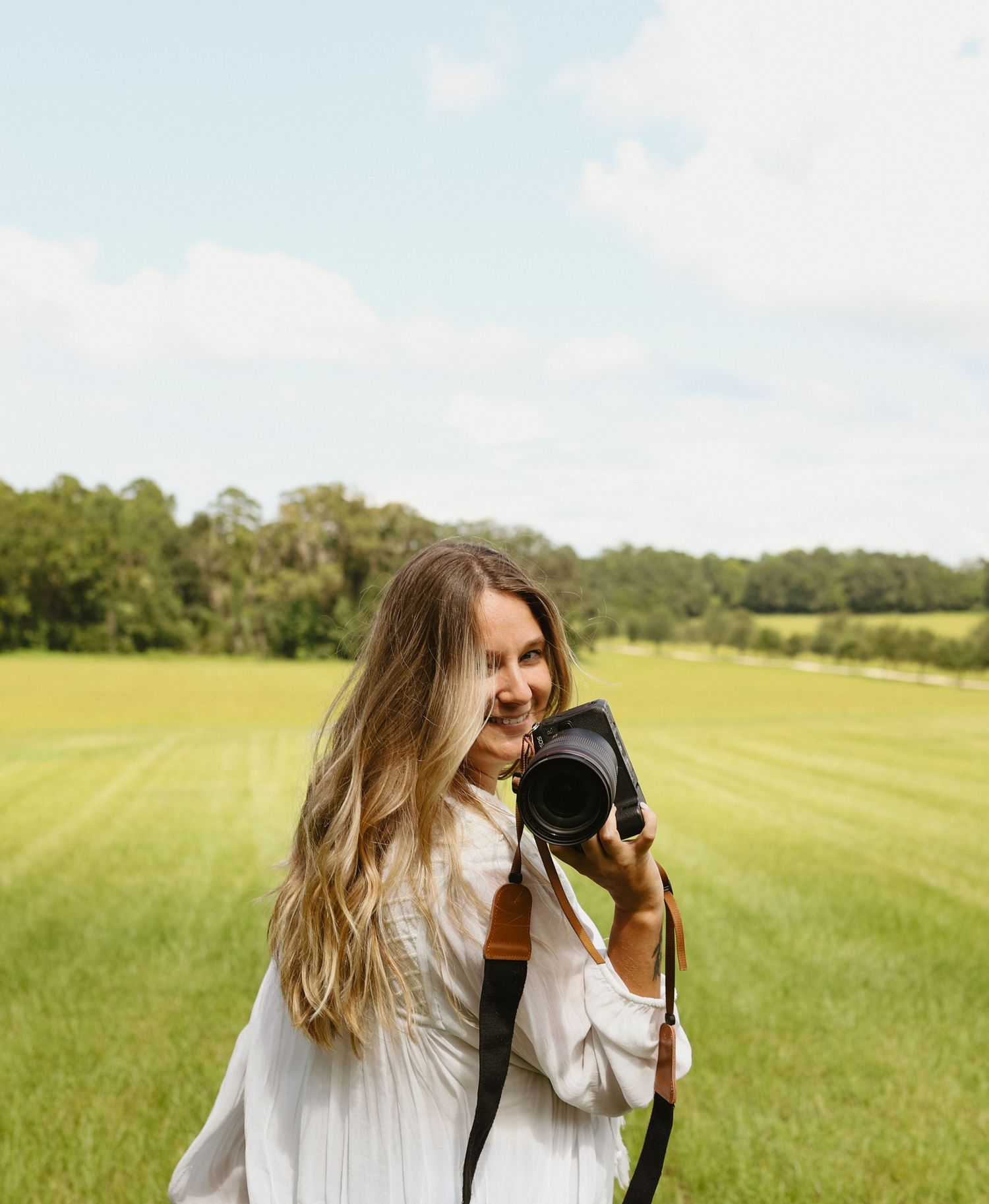 Person in white dress spinning with camera in sunny green field.