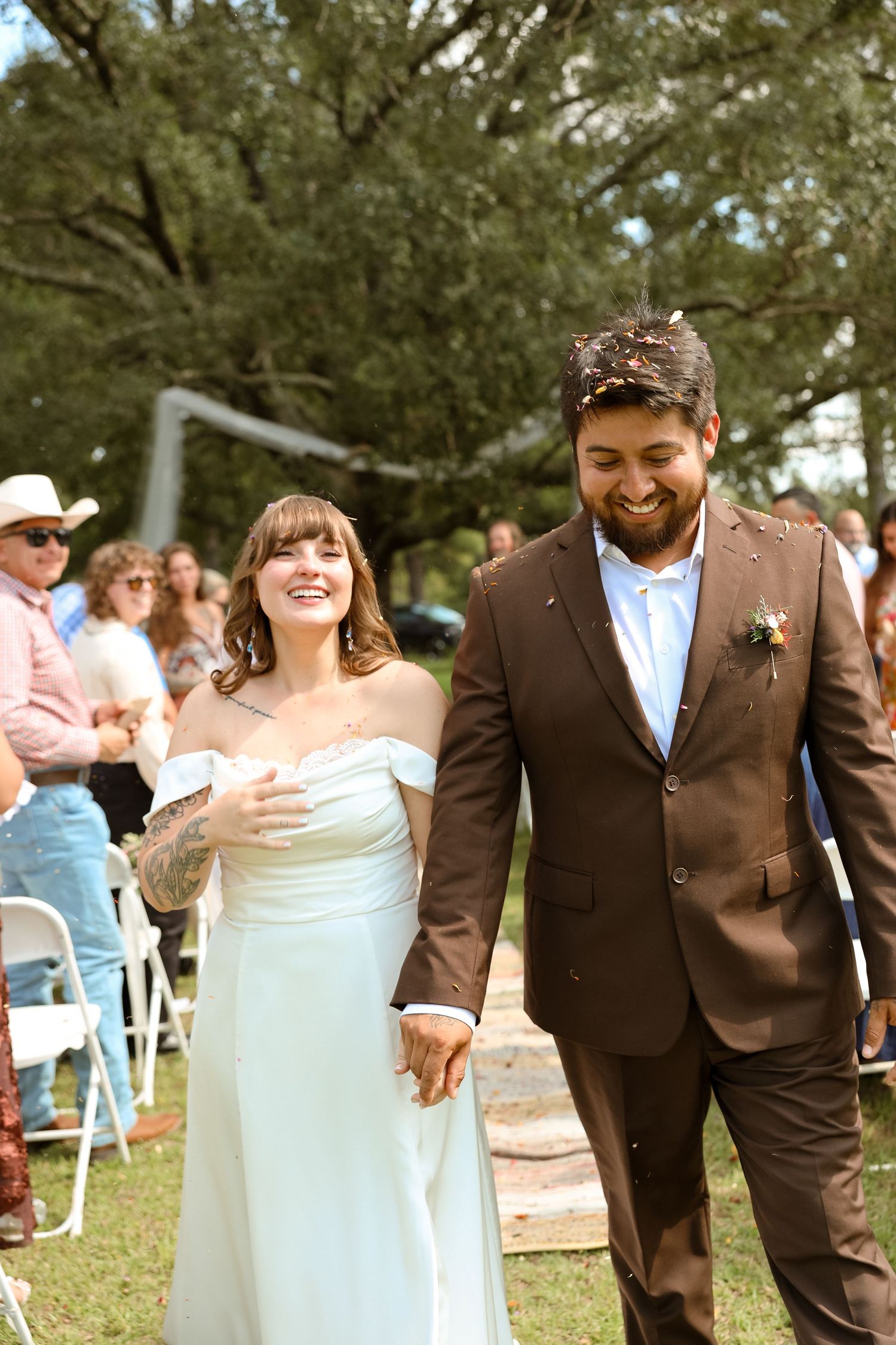 A joyful bride and groom walk hand in hand down the aisle at an outdoor wedding ceremony.