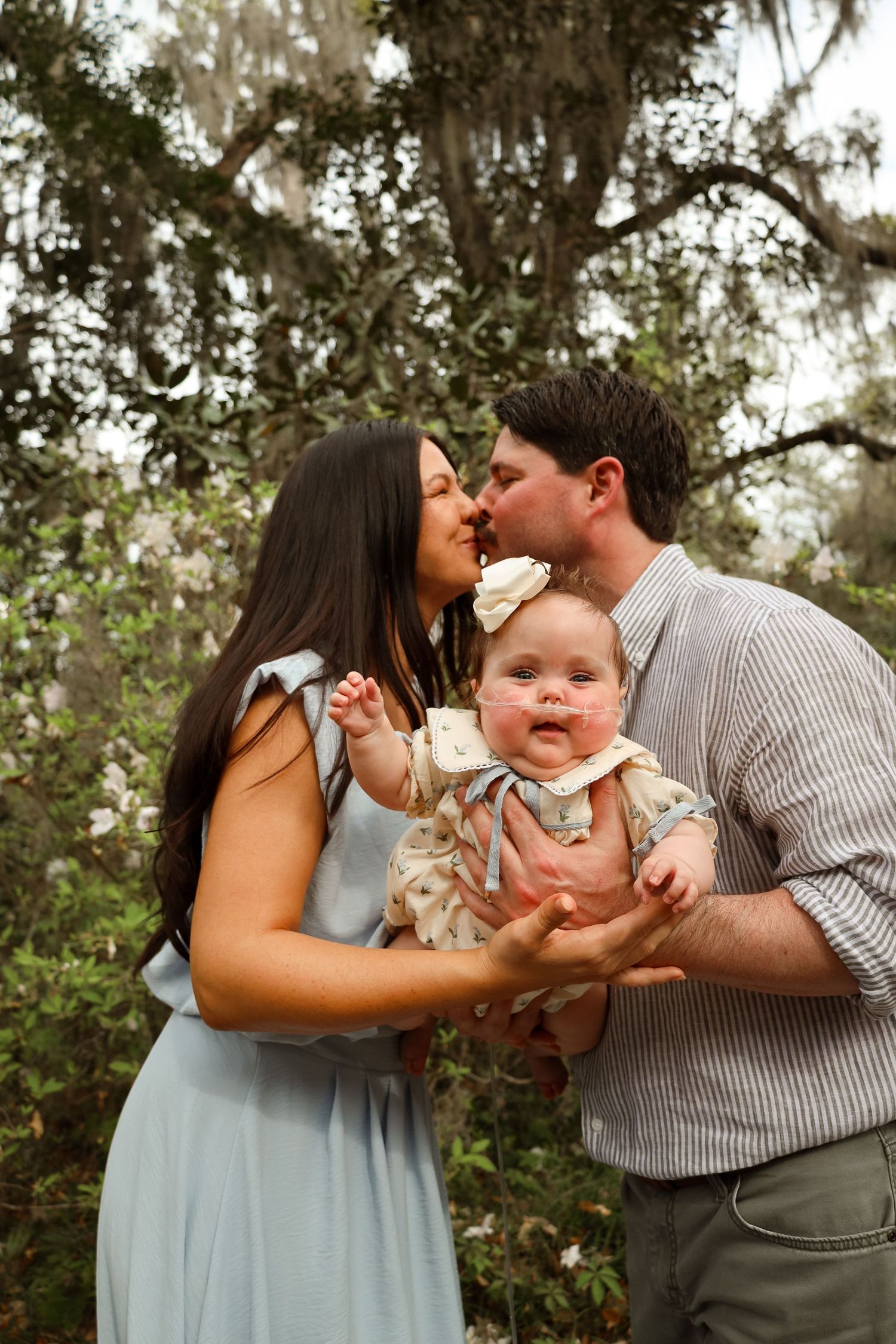 A couple shares tender moments with their baby in a series of outdoor family portraits set against a natural backdrop.