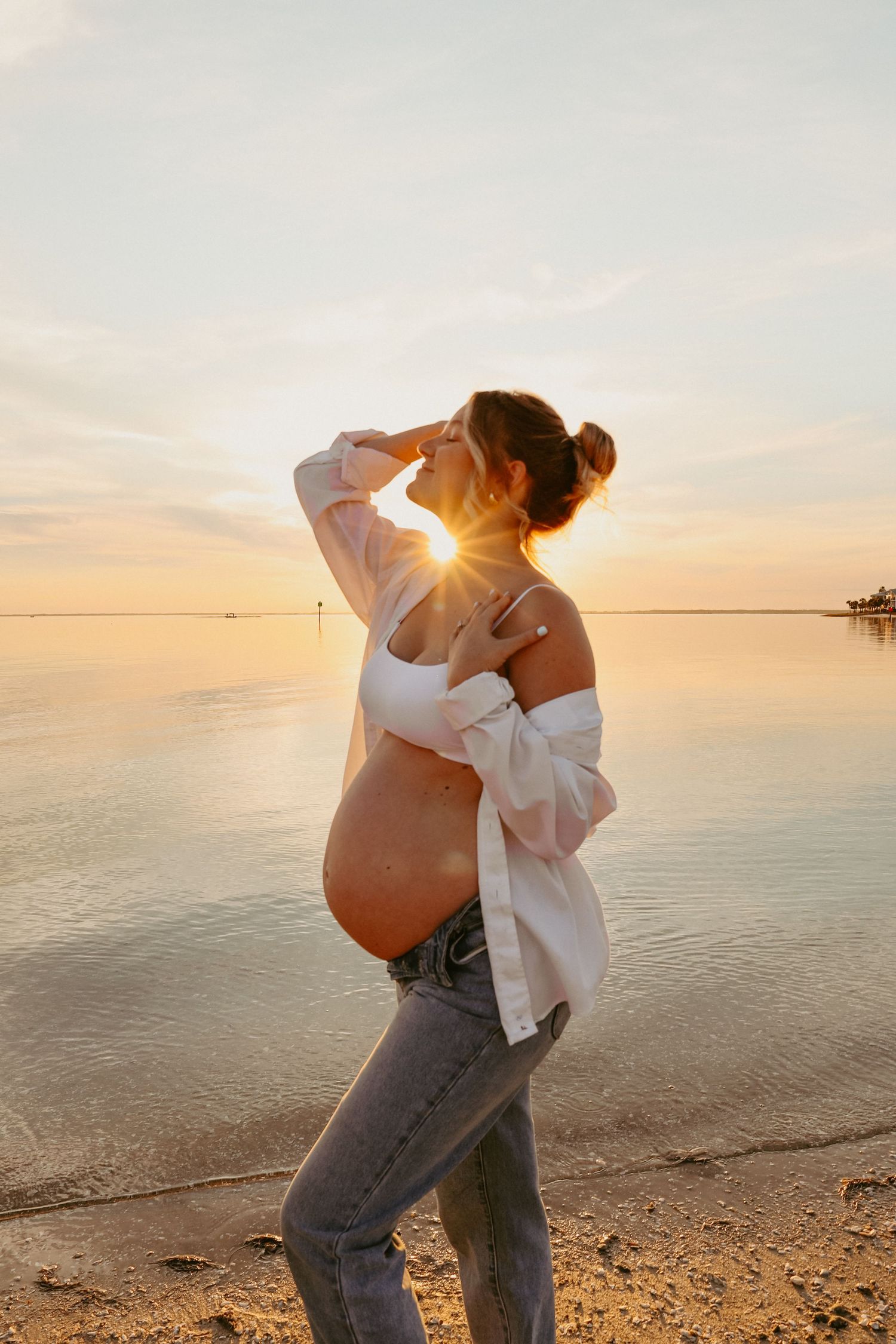 A couple embraces during their maternity photo session at the beach during golden hour.