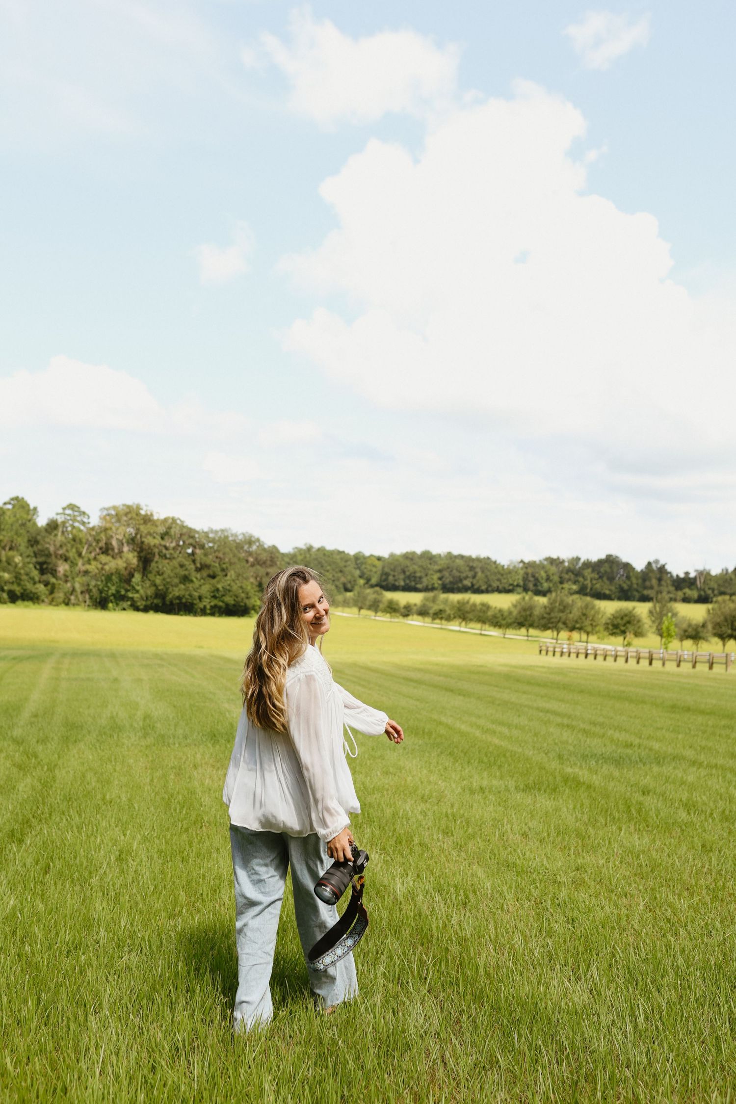 Person dancing freely in flowing white outfit across expansive green field.