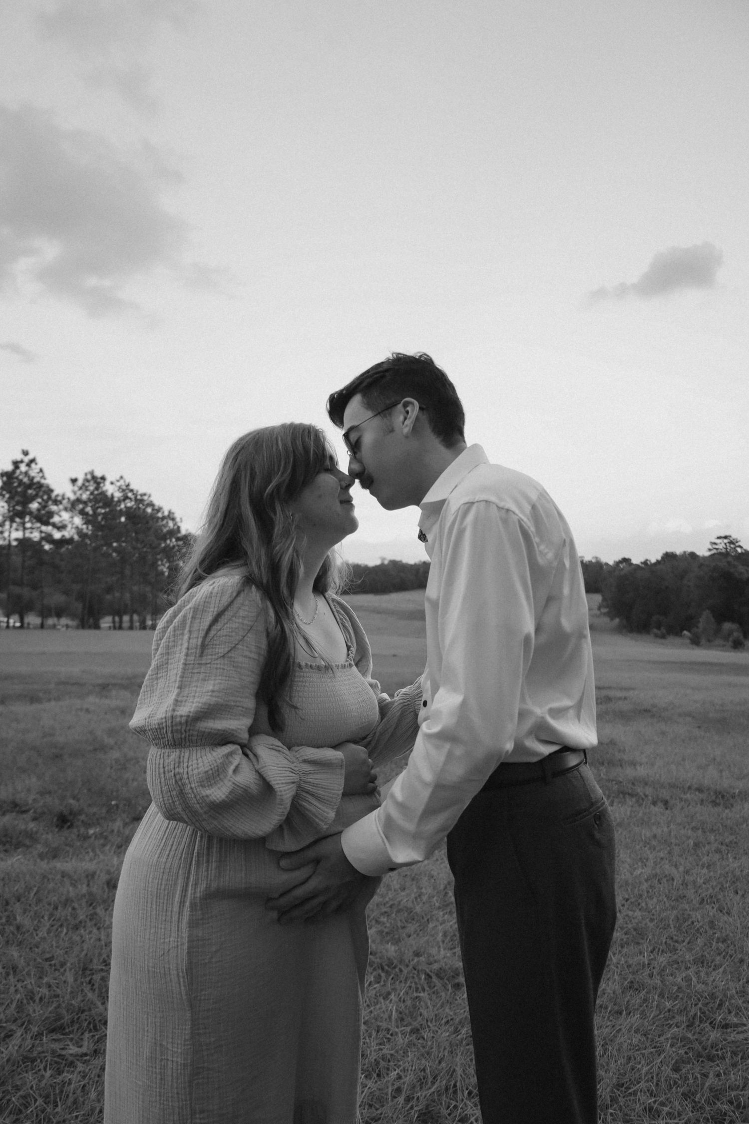 A romantic black and white photo series showing a couple embracing in a field at sunset.