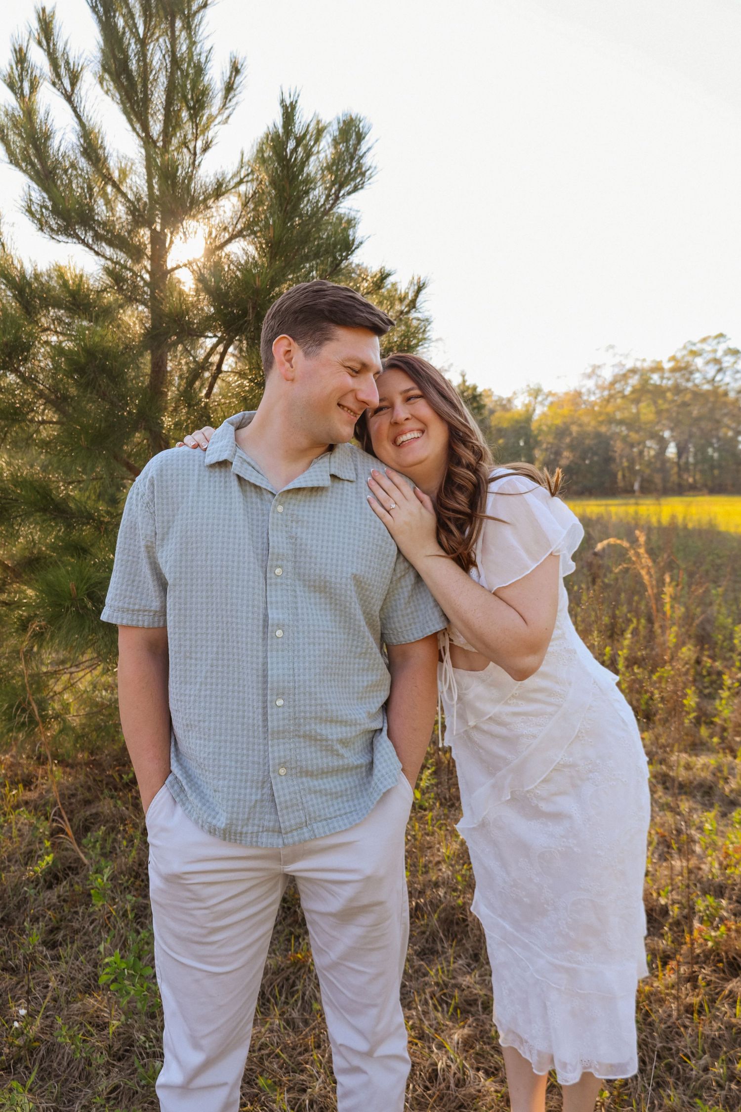 A couple shares a joyful moment together outdoors among pine trees during a sunset photo session.