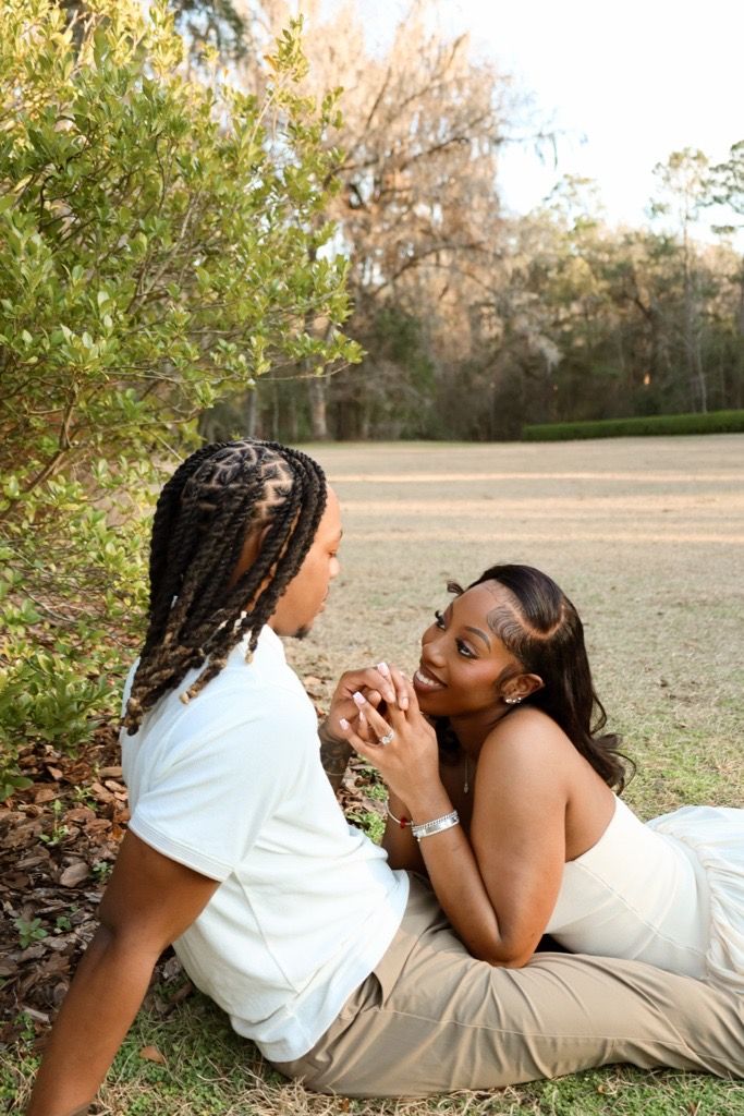 Two people lying on grass outdoors sharing a tender moment in natural lighting.