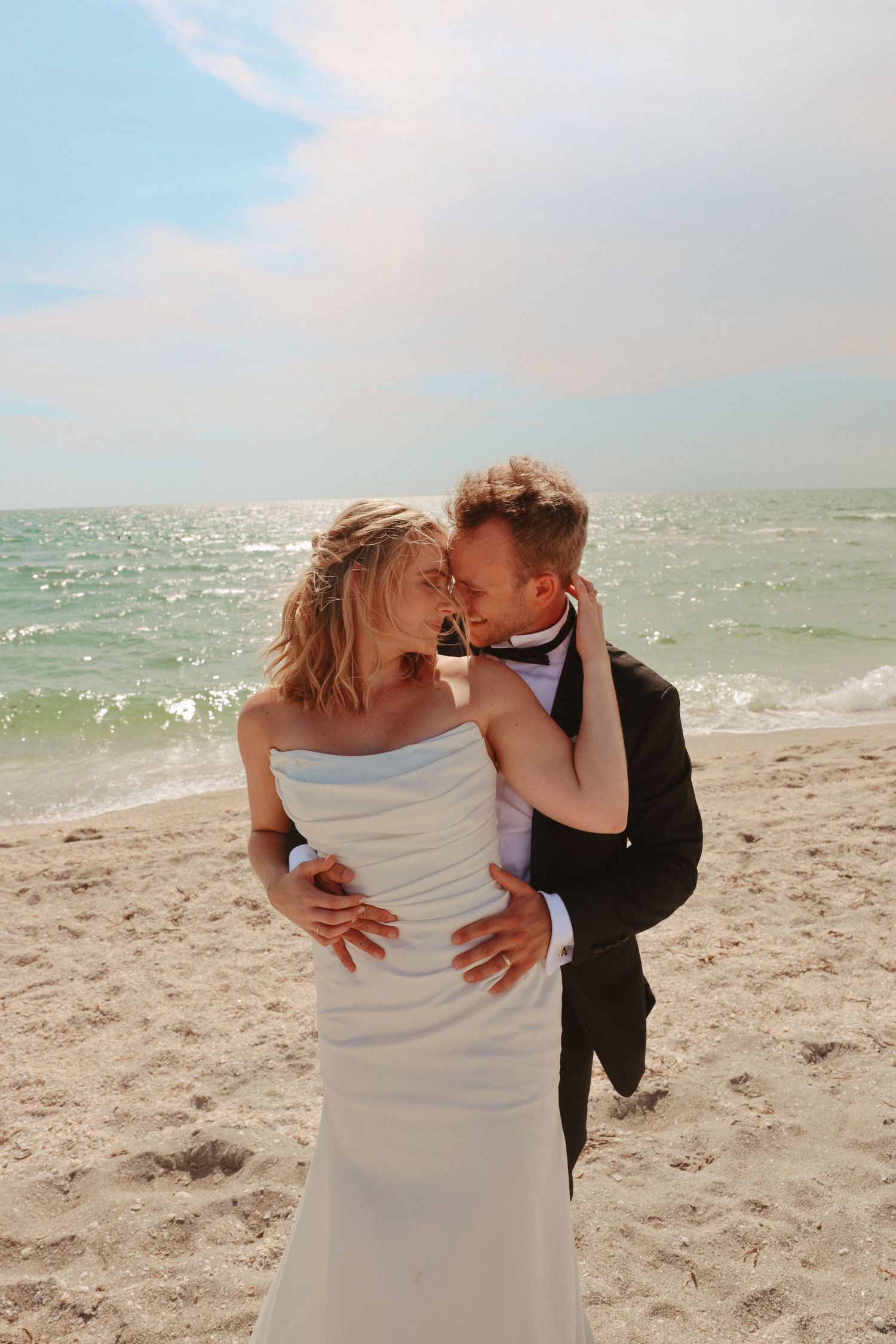 Couple shares romantic moment on beach with sparkling ocean waves in background.