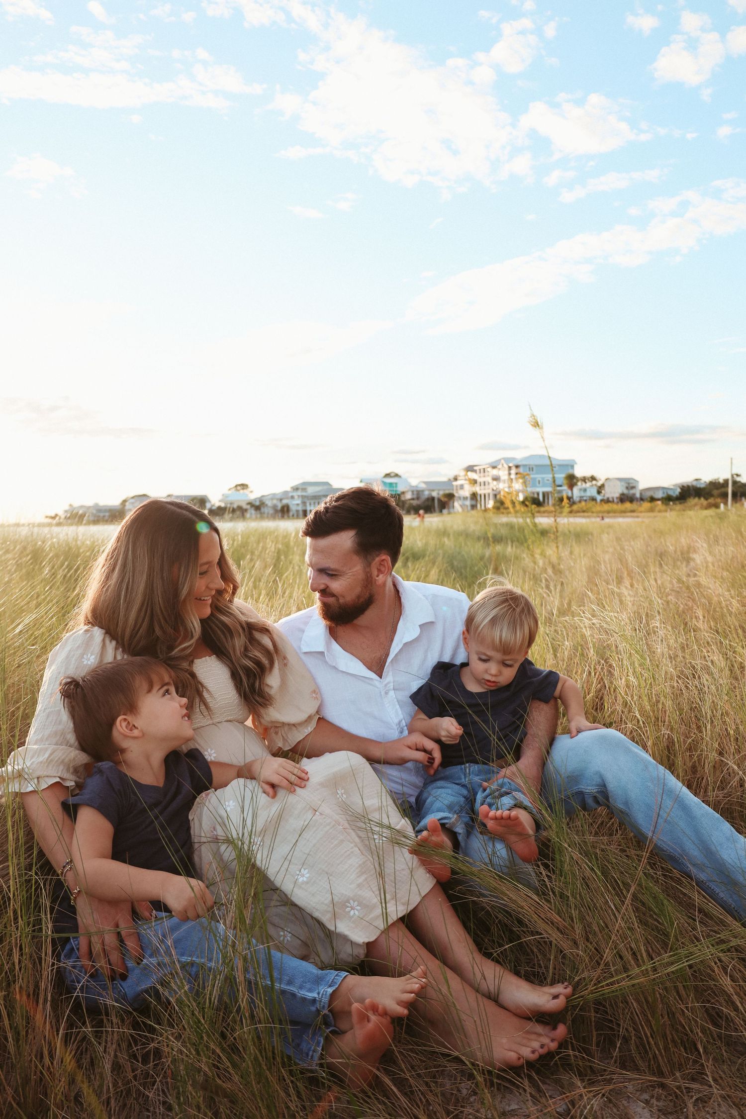A family sits together in a golden grass field on a sunny afternoon enjoying quality time outdoors.