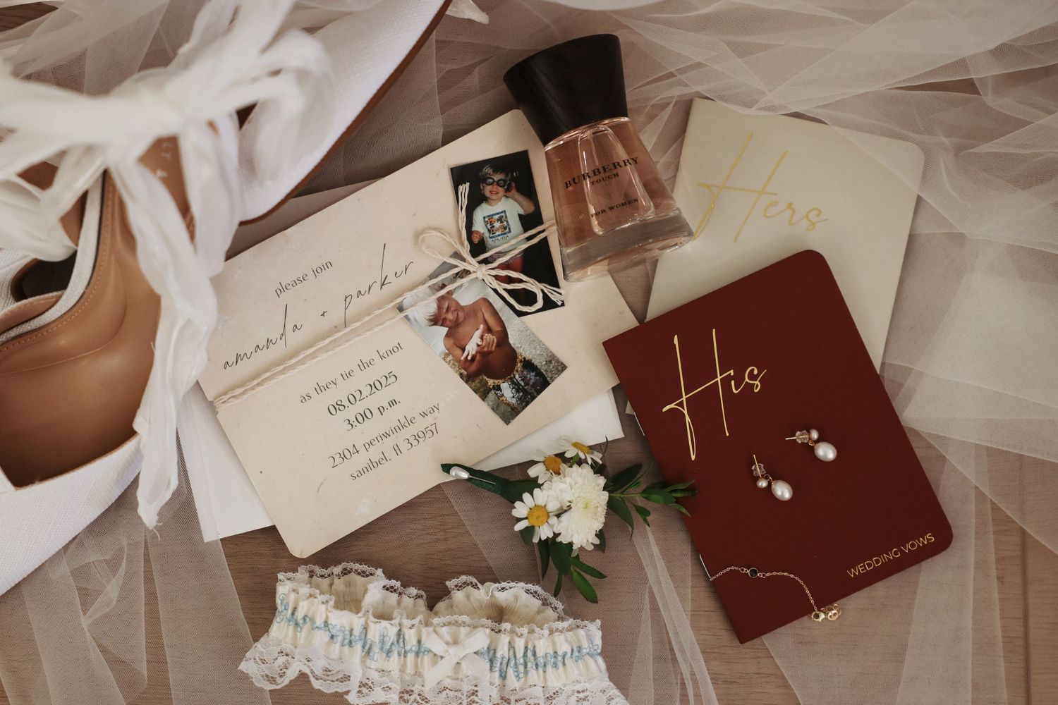 A collection of wedding details including rings, invitations, and delicate white tulle fabric arranged in a flat lay composition.