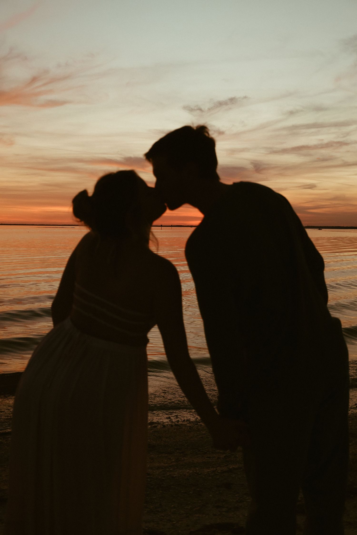 Silhouettes of a couple against a dramatic sunset sky at the beach.
