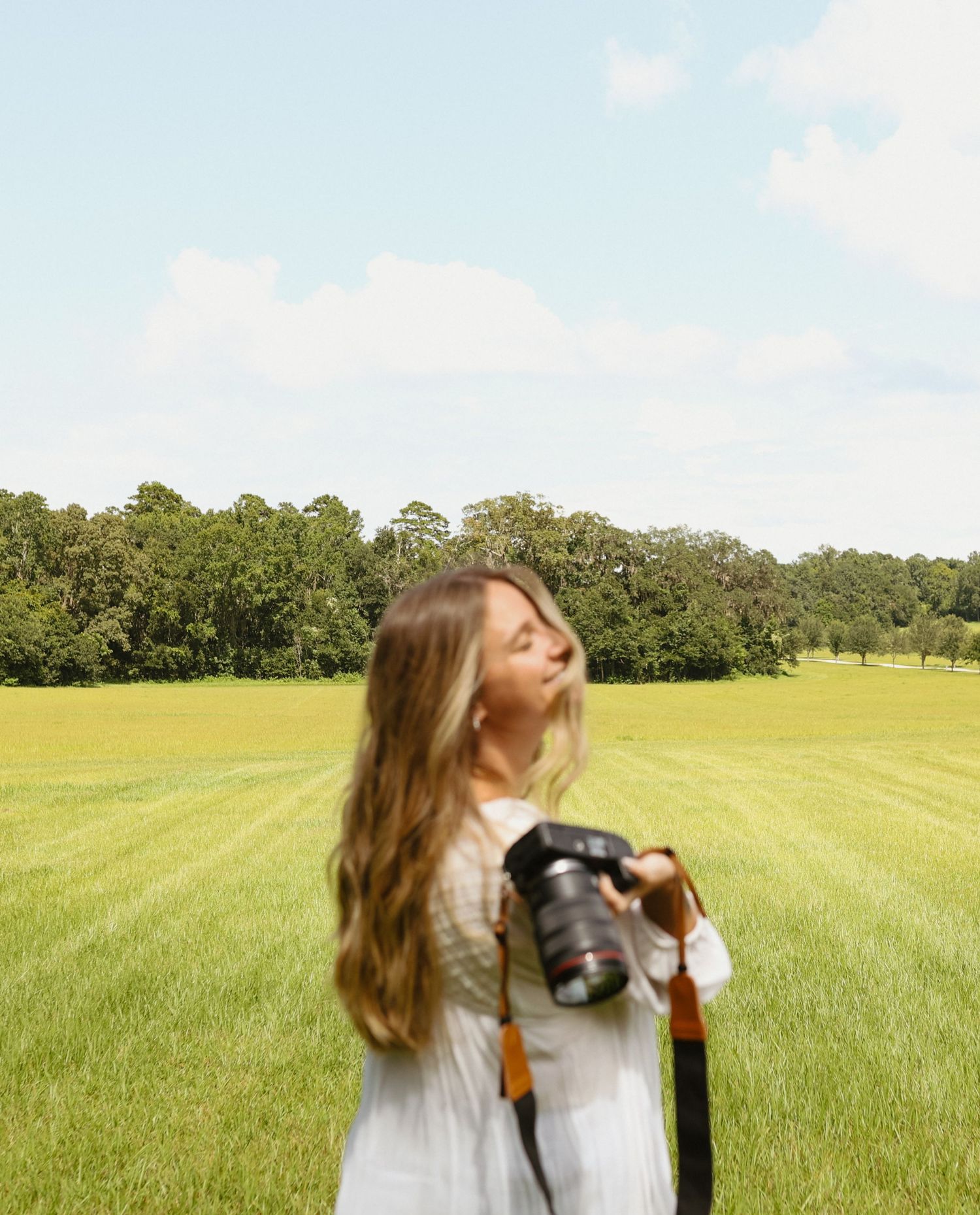 Person in white dress photographing in open field with dramatic movements.